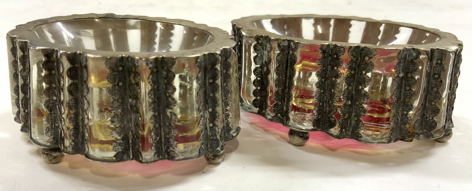 Silv Pl & Glass Pr Vintage Footed Salt Cellars: Lot includes 2 salt cellars each are glass with silver plated overlay. Each piece is footed with 4 feet each. Underside have cranberry toned. Each piece measures approximately 3 inches wide 2.25 inche