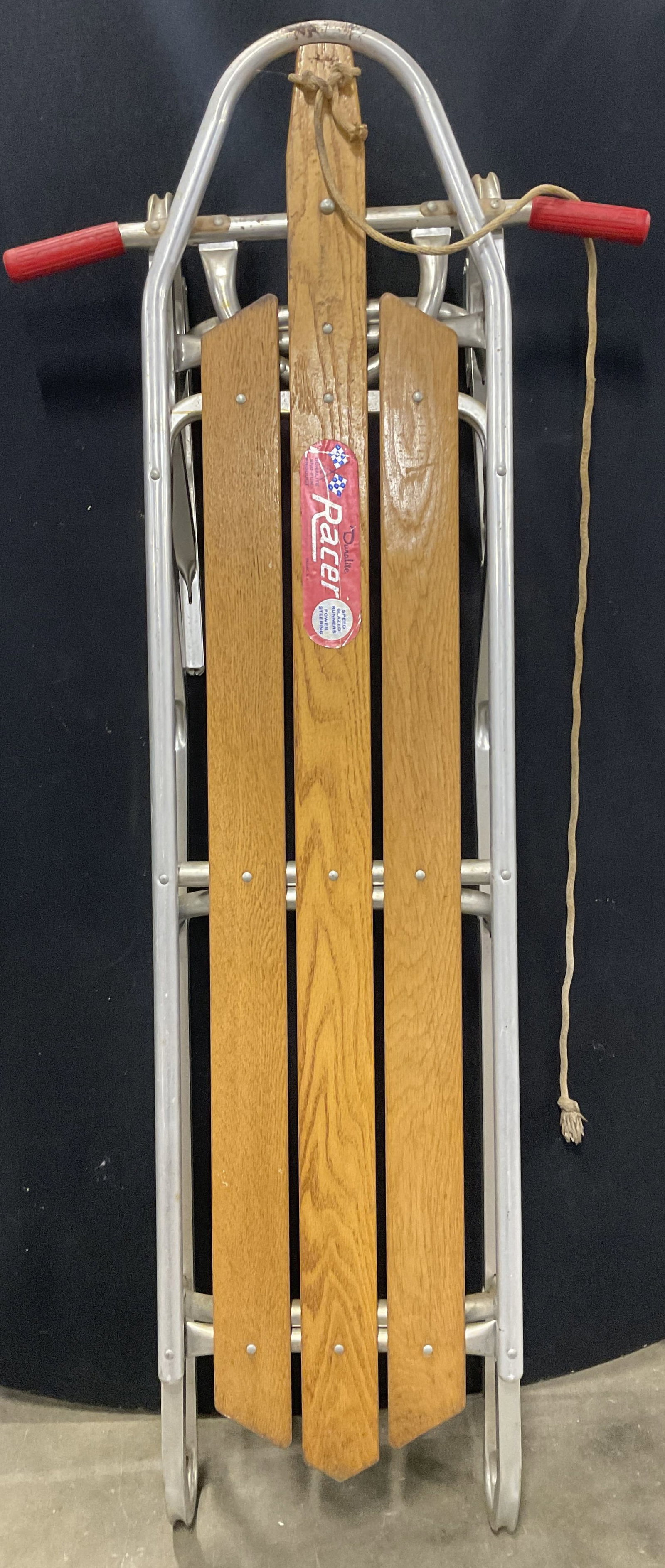 DURALITE RACER USA Vintage Wood & Metal Sled: DURALITE RACER USA Vintage Wood & Metal Sled. Rubber grips to the handles and a rope tied to the front. Tag to obverse reads DURALITE RACER, PASSAIC NJ, A DURALITE SNO FUN PRODUCT. Measures approx. 25