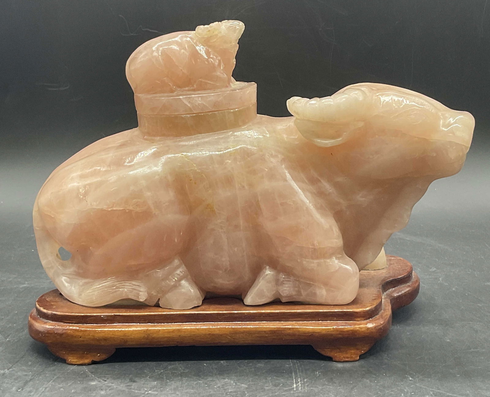 Pink Jade Lidded Bull Vessel W/ Wooden Stand: Pink Jade Lidded Bull Vessel With Wooden Stand. The stone is affixed to the wooden stand. The lid features a bull figural as well. Etched designs to the pieces. Measures approx. 6.25H x 8.25W in. Appe
