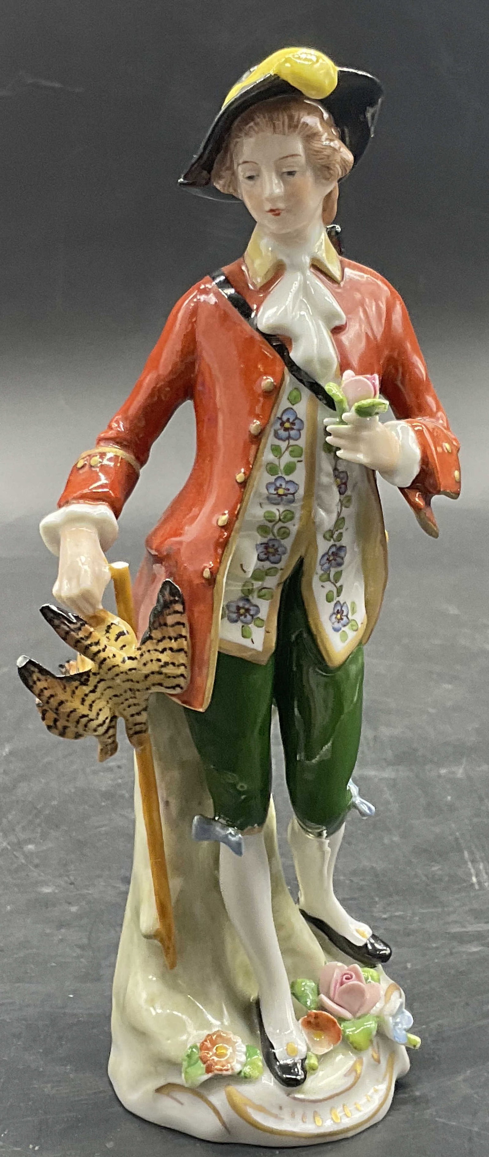 SITZENDORF German Porcelain Huntsman Figural: SITZENDORF German Porcelain Huntsman Figural. The subject is a man standing amongst raised florals. He holds deceased pheasants in one hand and a flower in the other. Hand painted details throughout. 