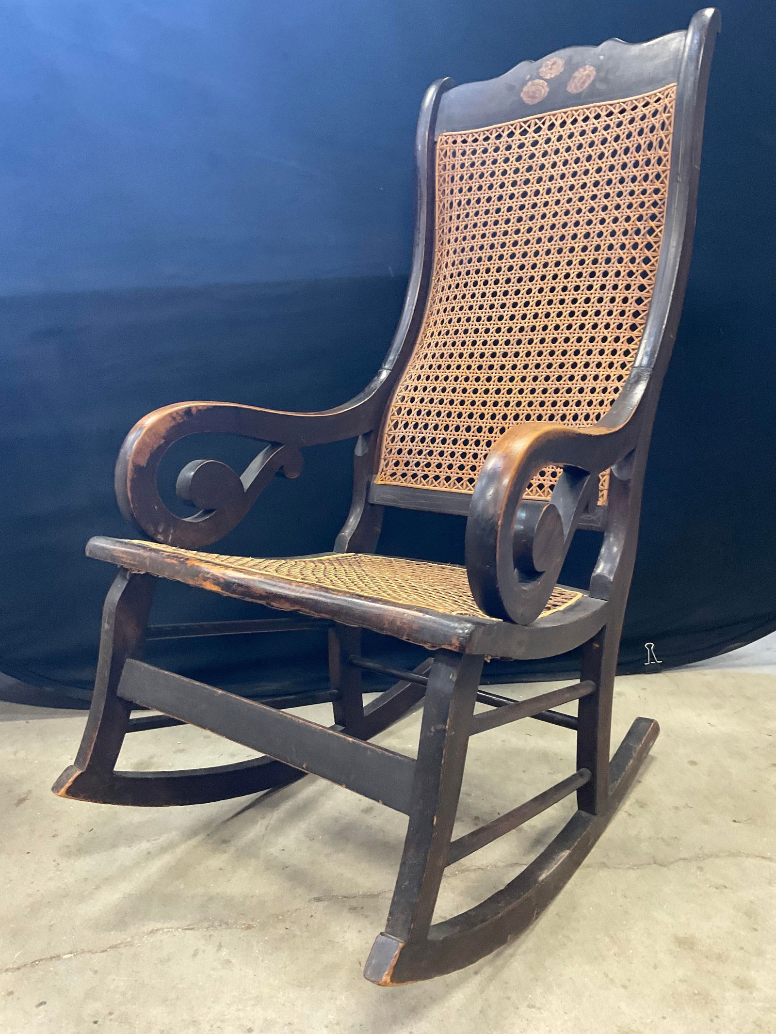 Vtg Floral Motif Caned Wooden Frame Rocking Chair: Vintage Floral Motif Caned Wooden Frame Rocking Chair. Caned seat and back. Scrolled arms. Painted floral motif to the top. Measures approx. 22W x 29D x 42H in. Measured at deepest point. Losses, disc