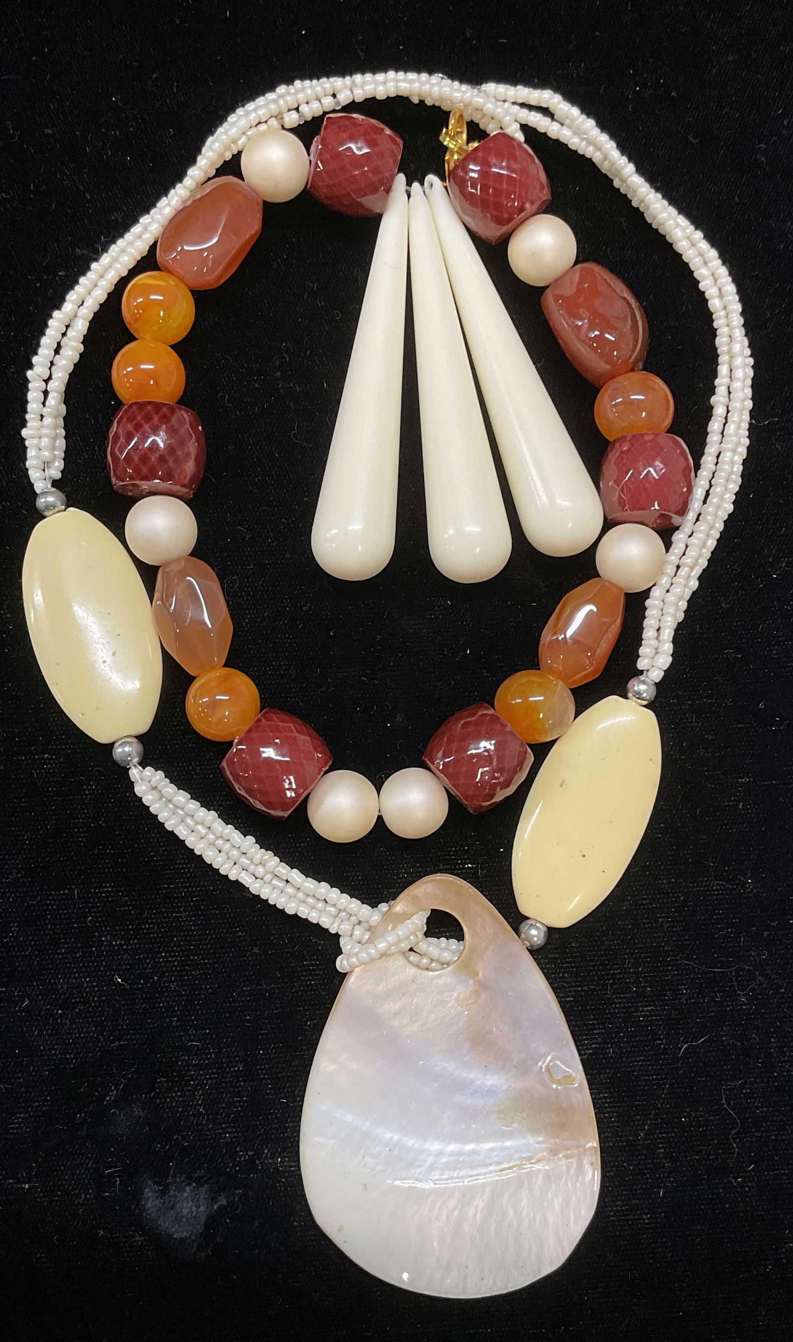 Lot 2 Mother of Pearl Pendant Necklace +: Lot of 2 necklaces. Mother of pearl pendant necklace with seed bead and lucite. Orange agate, lucite, and faux pearl beaded necklace. Longer drop length approx 7.5 inches. One clasp needs repair. Both