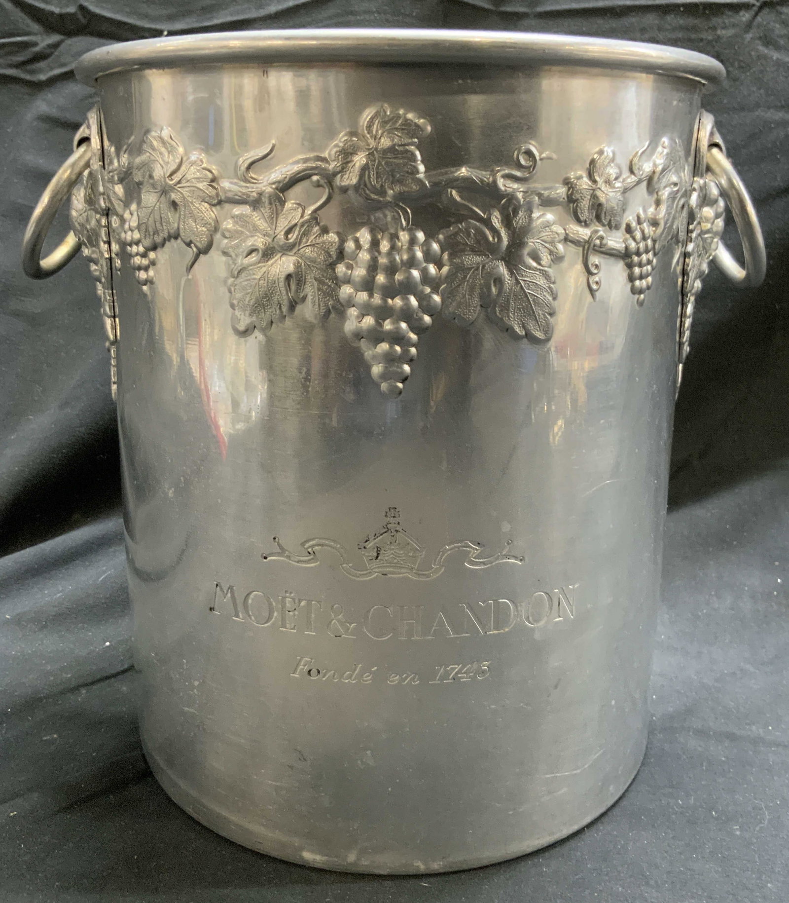 MOET & CHANDON Brushed Metal Champagne Bucket France: Front of piece is inscribed MOET & CHANDON. Piece is silver toned brushed metal. Champagne bucket has grape, vine and leaf detail. Piece has loop form handles. Underside inscribed MADE IN FRANCE. Cham