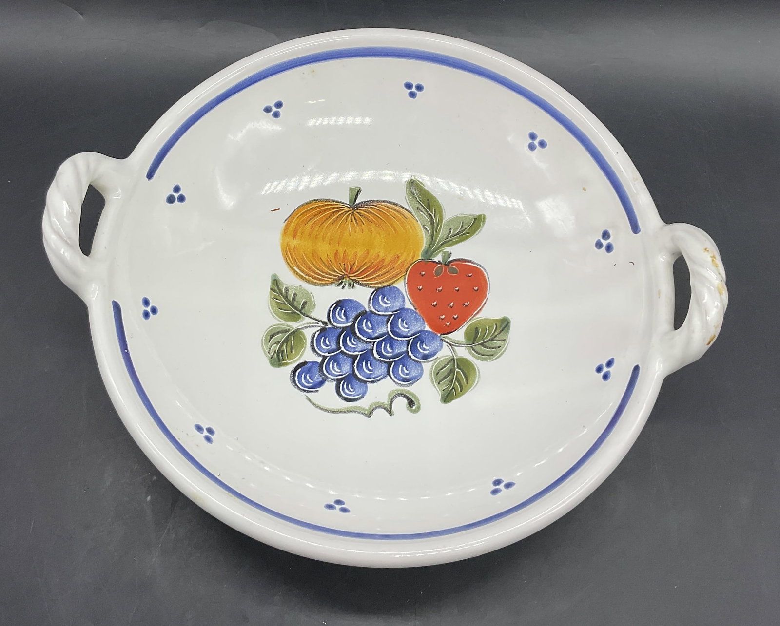 Handmade Glazed Fruit Motif Pottery Bowl: Handmade Glazed Fruit Motif Pottery Bowl. Multicolored fruit motif to the center. Twin handles to either side. Measures approx. 3.5H x 10.75W in. Discoloration, pitting, residue, crazing, and surface 