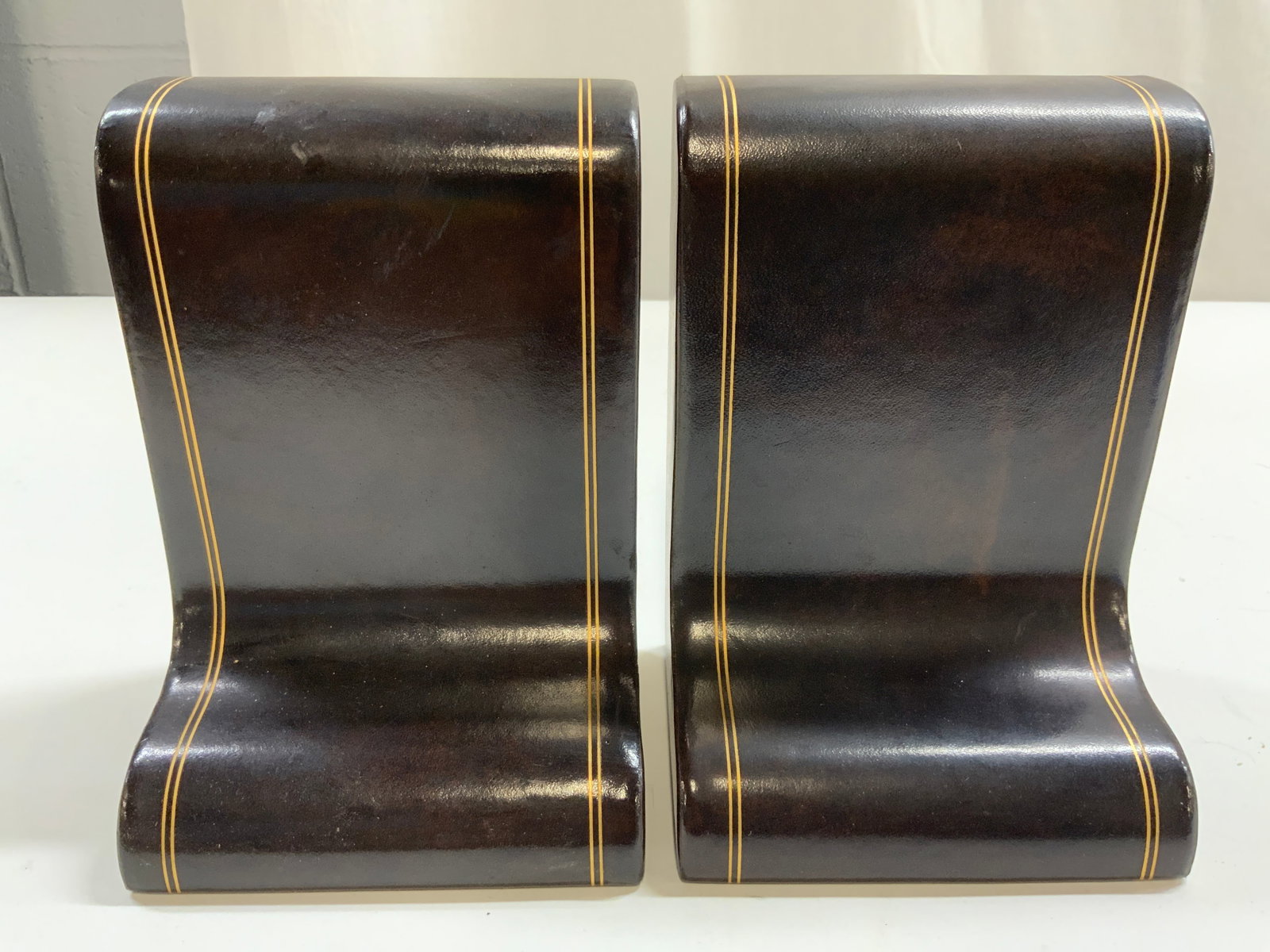 Pr Leatherette Lined Bookends W Gilt Stripes: Bookends are brown toned. Each piece is lined with leatherette material, possibly leather. Each piece has gilt piping at sides. Undersides are lined with brown toned felt. Bookends measure approximate