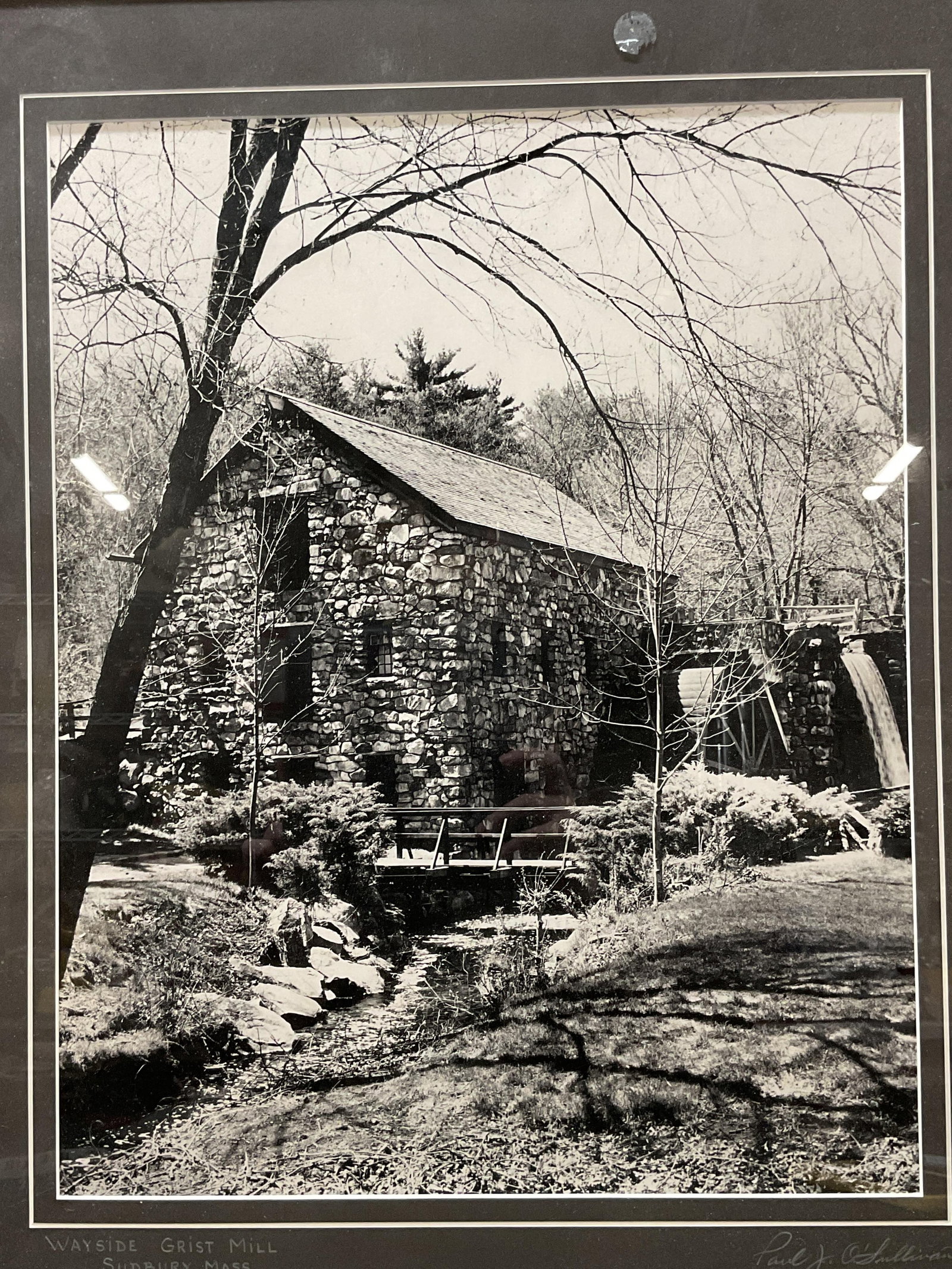 Sgn Paul Sullivan Wayside Grist Mill B&W Print 2ft: Framed and matted hand enlarged black and white photographic print. Wayside Grist Mill, Sudbury, Massachusetts by Paul O Sullivan. Signed on the mat ant lower right. Artist label on verso. Black frame