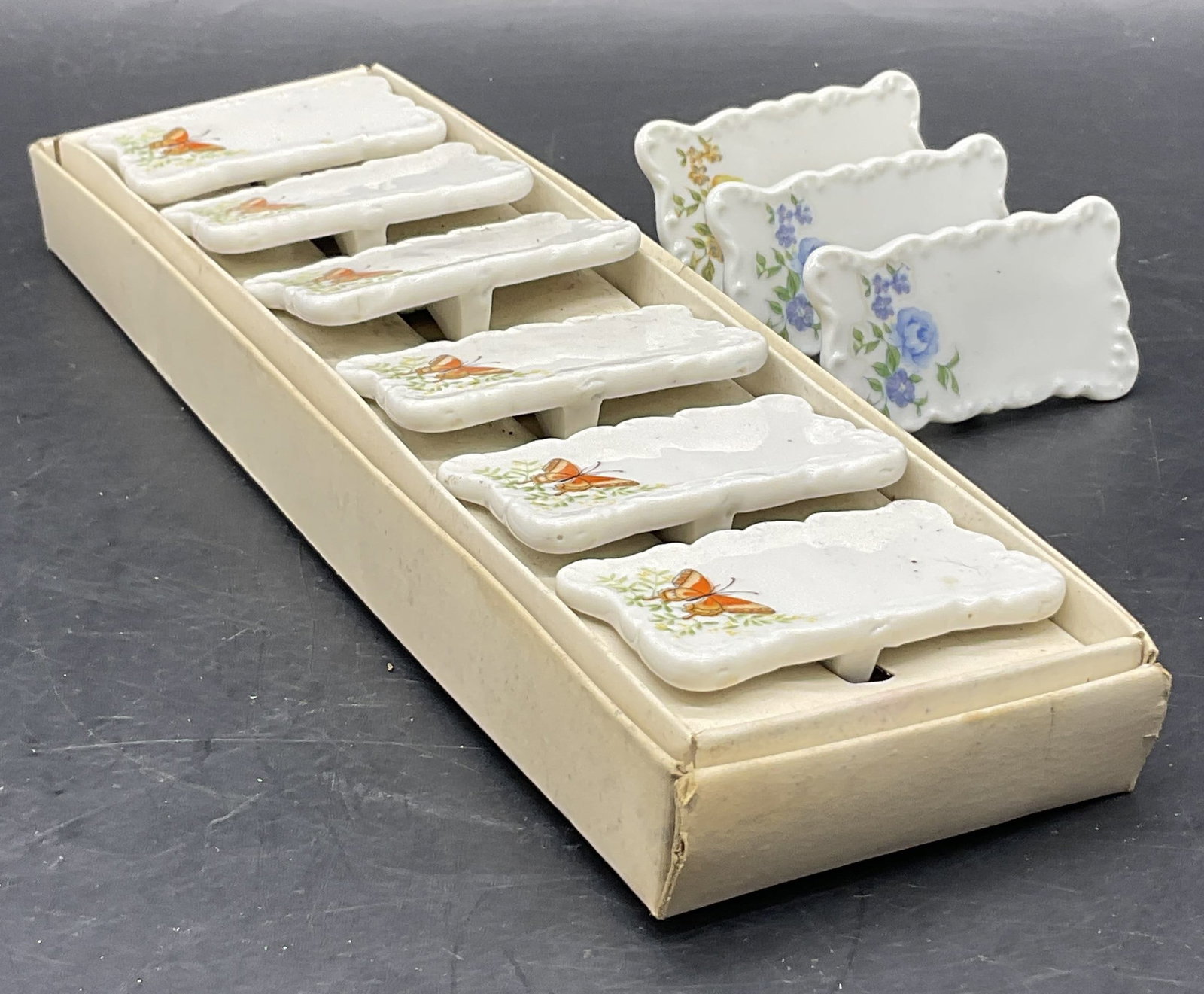 9 Vintage Porcelain Floral & Butterfly Place Cards: A lot of Nine Vintage Porcelain Floral & Butterfly Motif Place Cards. The butterfly place cards come with a box. Box measures approx. 9.75L x 3W in. Losses and surface wear to the box. Place cards hav