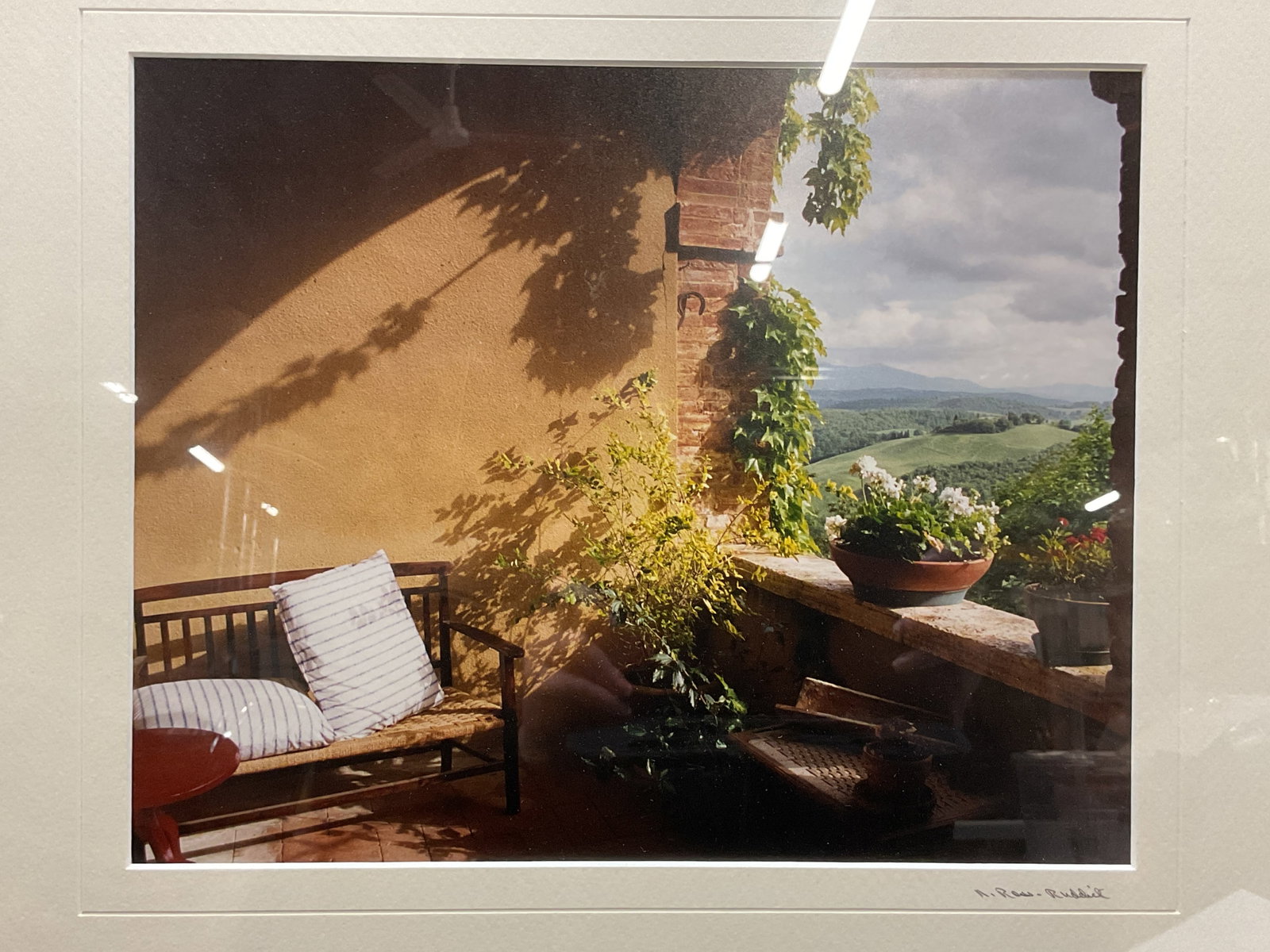 Signed N Ross Ruddick Fine Art Photo Print: Framed and matted fine art photography print. Signed N Ross Ruddick on mat at lower right, exterior scene with bench and plants on balcony. Wood frame. Not examined out of frame. Frame measures approx