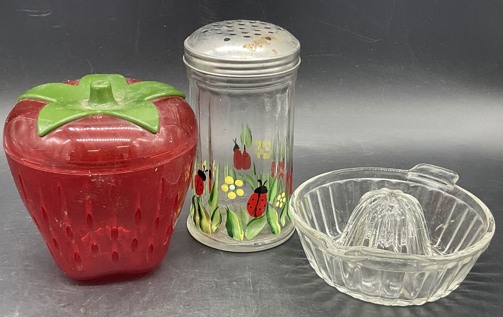 3 Vintage Kitchenware Accessories, Glass Juicer+: A lot of three vintage kitchenware accessories. Includes a glass juicer, a pierced plastic lidded strawberry storage vessel, and a glass & metal ladybug motif seasoning shaker. The shaker measures app