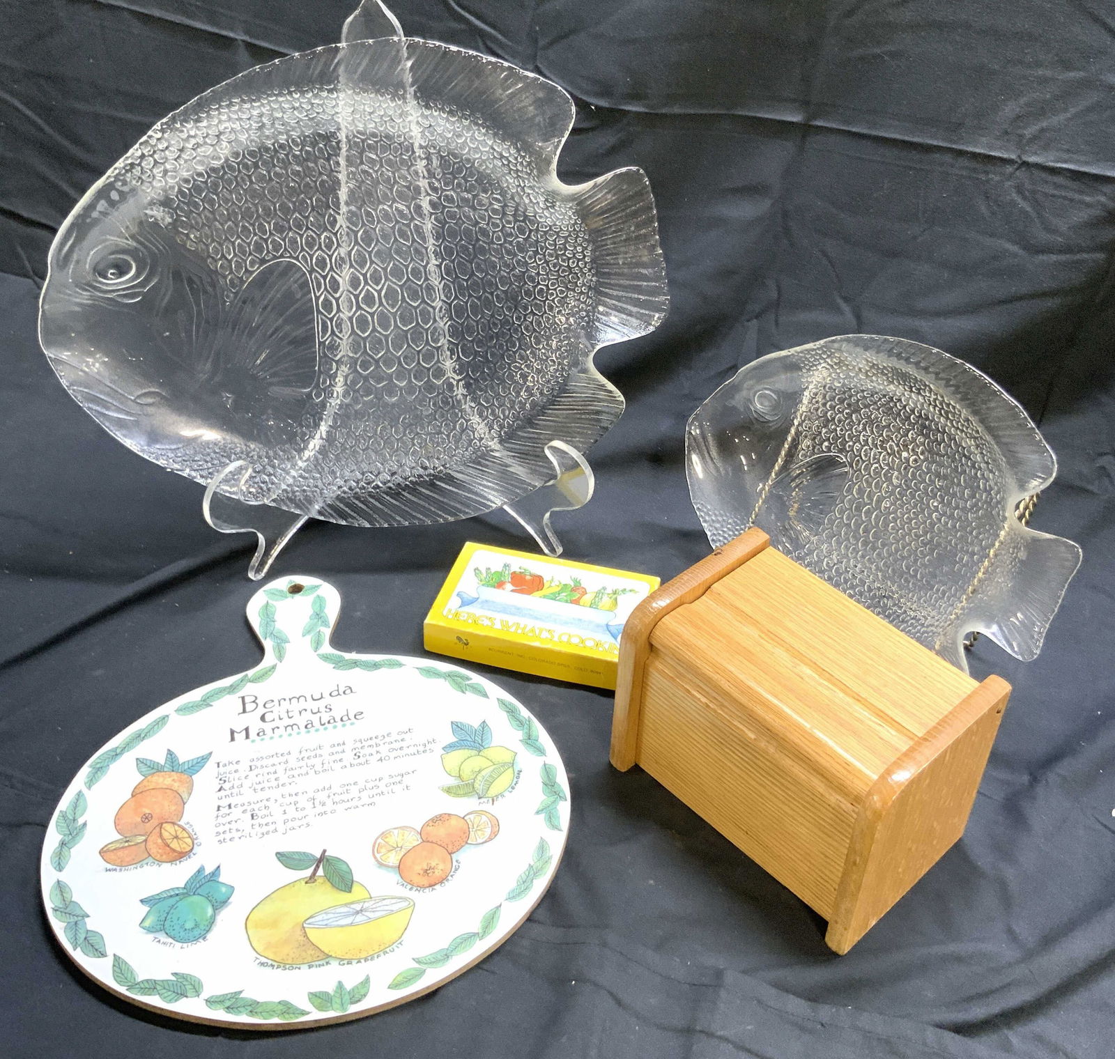 Lot 5 Gls Fish Dishes & Kitchenware Accessories: Lot includes 1 wooden box with lid, 1 box of recipe cards, 2 art glass fish form serving dishes, & 1 cutting board with handle & Bermuda Citrus marmalade recipe. Largest fish serving plate measures ap