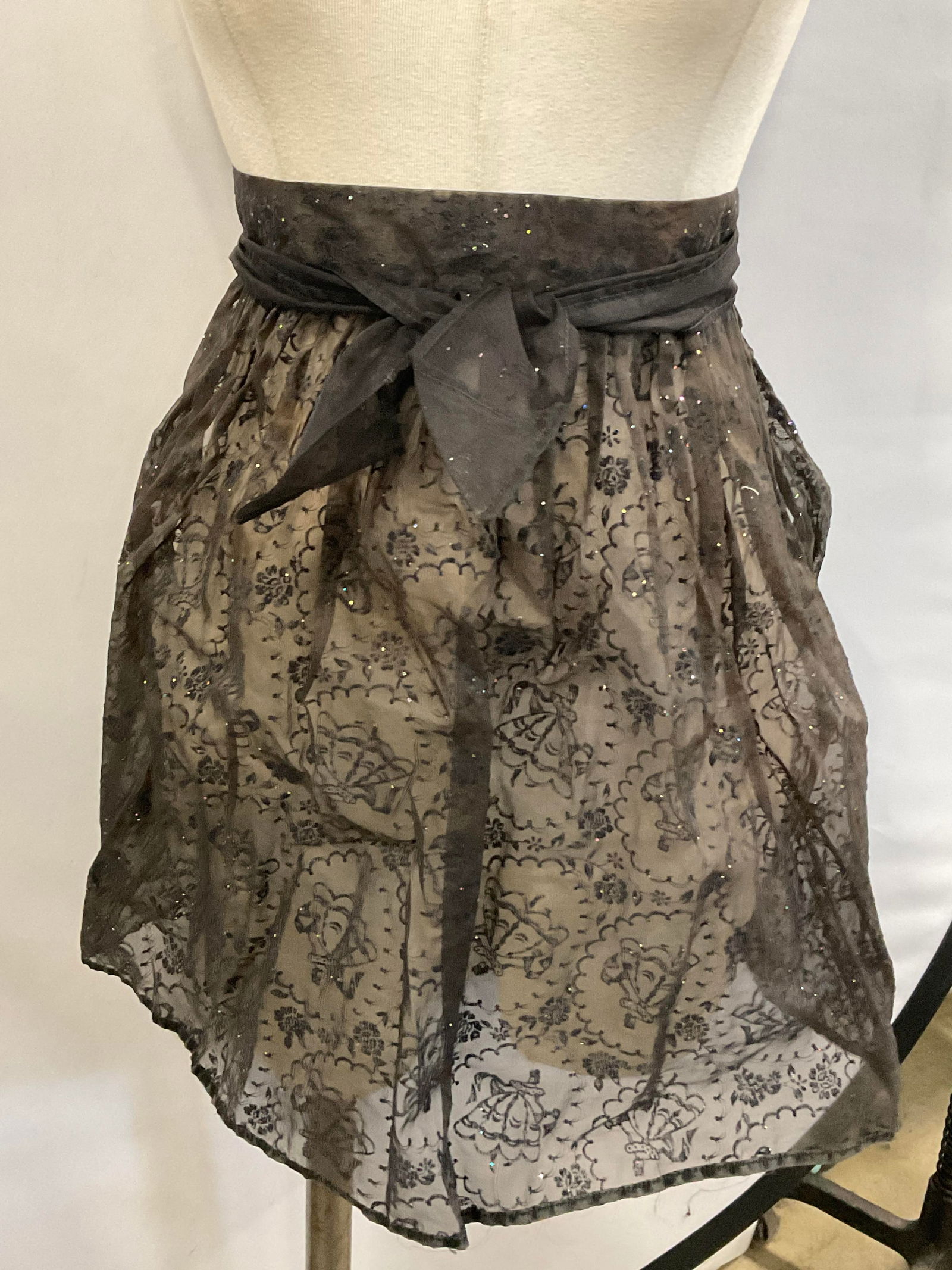 Vntg Sparkled Black Fabric Tie Waist Skirt Apron: Vintage Sparkled Black Fabric Tie Waist Skirt Apron. Black-gray hued fabric with a floral motif to the skirt. Tie waist measured end to end approx. 60 inches in length. Loose threads, surface wear, an