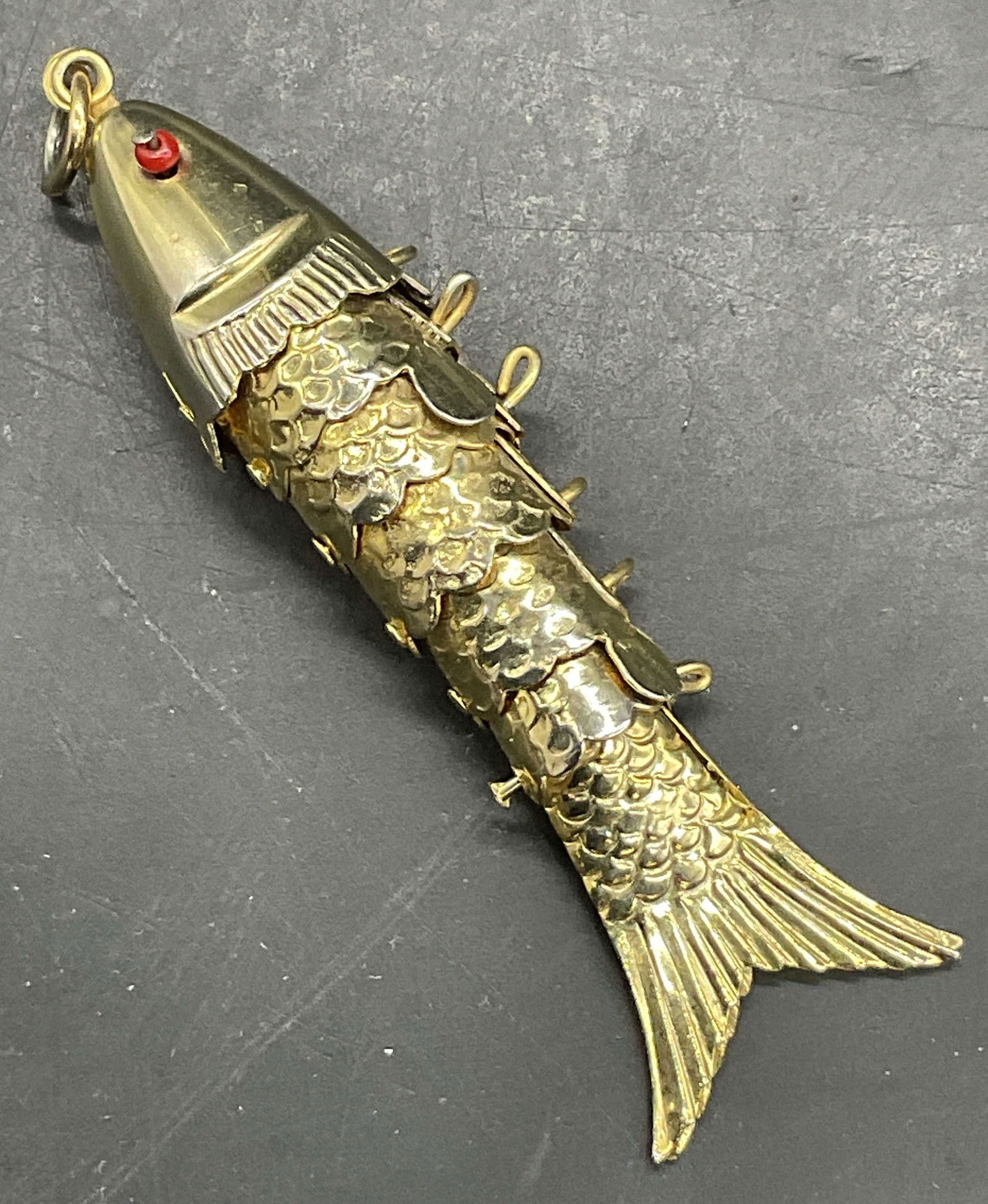 Articulated Enameled & Beaded Metal Fish Pendant: Articulated Enameled & Beaded Metal Fish Pendant. Crafted from gold tone metal and accented by green enamelwork and red beads. Measures approx. 2.5W x .5L in. Surface wear consistent with age, use, an