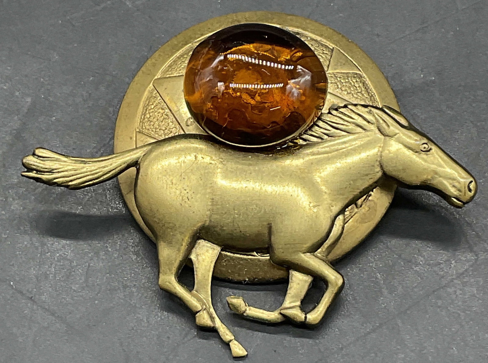 Vintage Costume Amber Cabochon Horse Motif Pin: Vintage Costume Amber Cabochon Horse Motif Pin. Gold tone metal with a costume cabochon to the obverse. Metal pin closure to the reverse. Measures approx. 2.W x 1.5L in. Glue residue and surface wear 