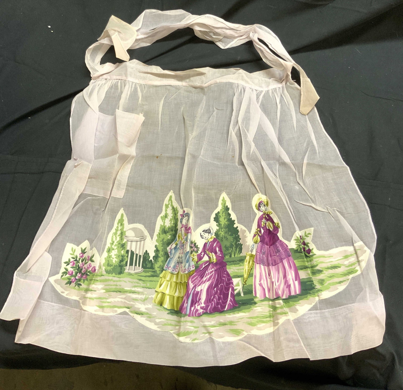 Vintage Polyester Patchwork Apron W Female Figures: Apron is vintage. Piece appears to be polyester. Apron is pink with patchwork depicting female figures in a landscape setting. Piece measures approximately 19.5 jnch3s tall 25 inches wide. Apron, poly