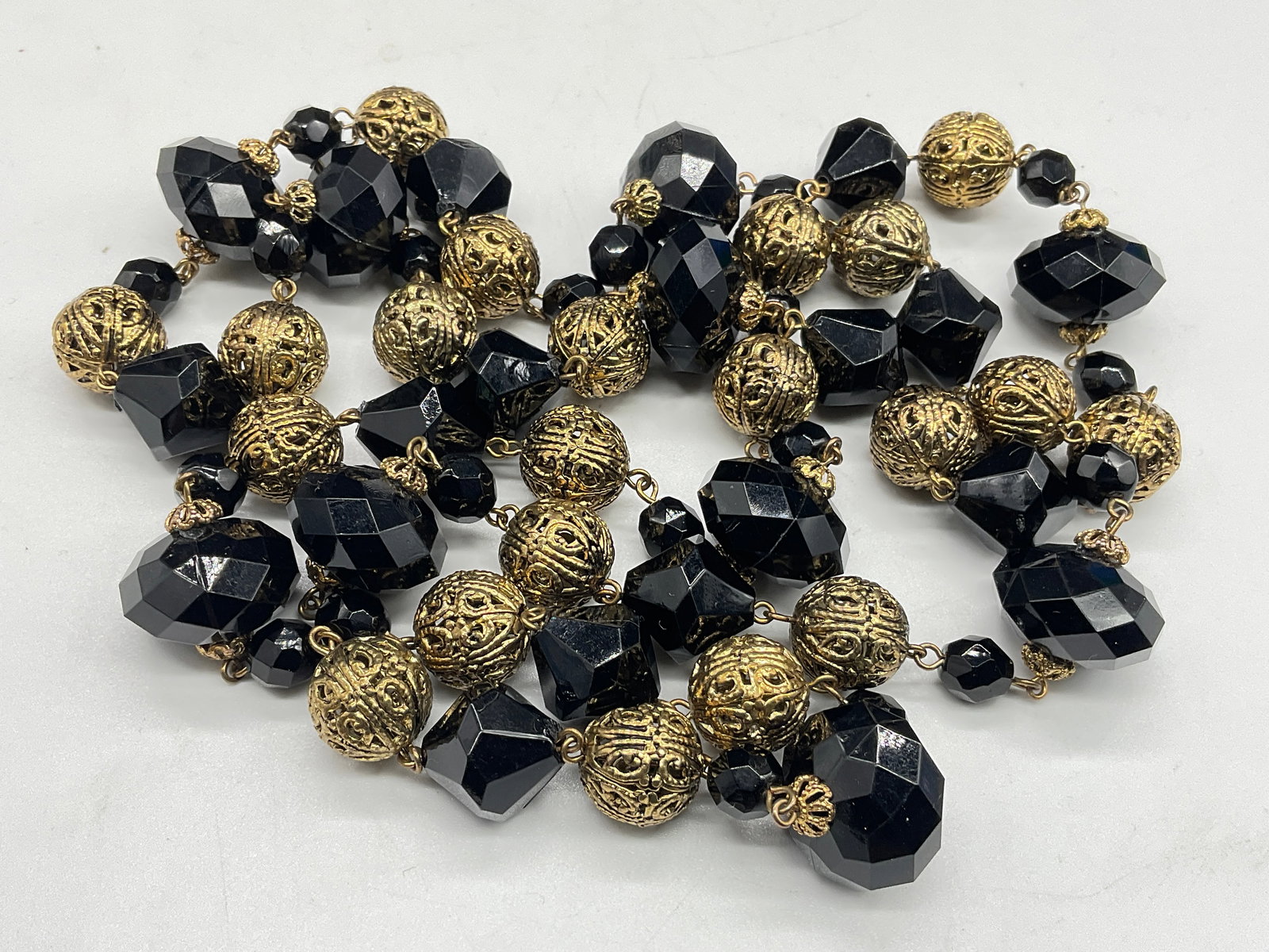 Vtg Gold Tone Metal & Black Faceted Bead Necklace: Vintage Gold Tone Metal & Black Faceted Bead Necklace. The gold tone metal beads featured pierced / open metalwork designs. The composite black beads are faceted. Necklace length measured end to end a