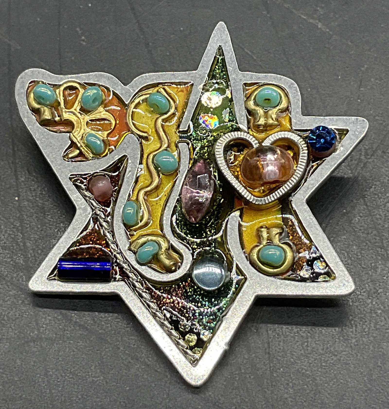 Vintage Bejeweled Abstract Star of David Brooch: Vintage Bejeweled Abstract Star of David Judaica Brooch. Silver tone metal brooch featuring faceted crystals, beads, and enamelwork. Metal pin closure to reverse. Measures approx. 1.25L x 1.25W in. Su