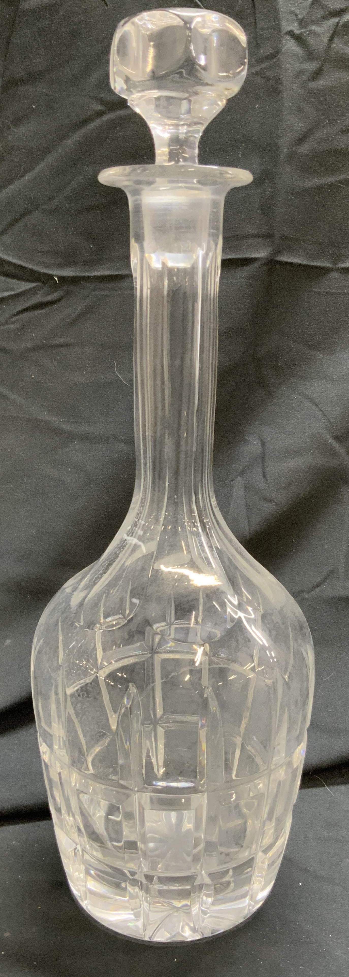 Crystal Art Glass Decanter W Stopper: Decanter is crystal. Piece has geometric relief detail around base. Decanter includes stopper. Decanter rim leans outward. Piece includes stopper. Decanter measures approximately 13 inches tall 4.5 in