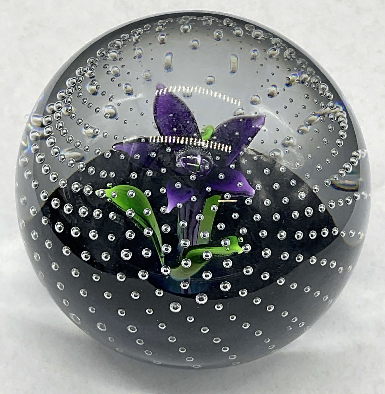 CAITHNESS SCOTLAND Flower In The Rain Paperweight: CAITHNESS SCOTLAND Flower In The Rain Art Glass Paperweight. Colorless glass featuring a purple floral and bubbles to the interior. Underside signed CAITHNESS SCOTLAND Flower In The Rain. Measures app