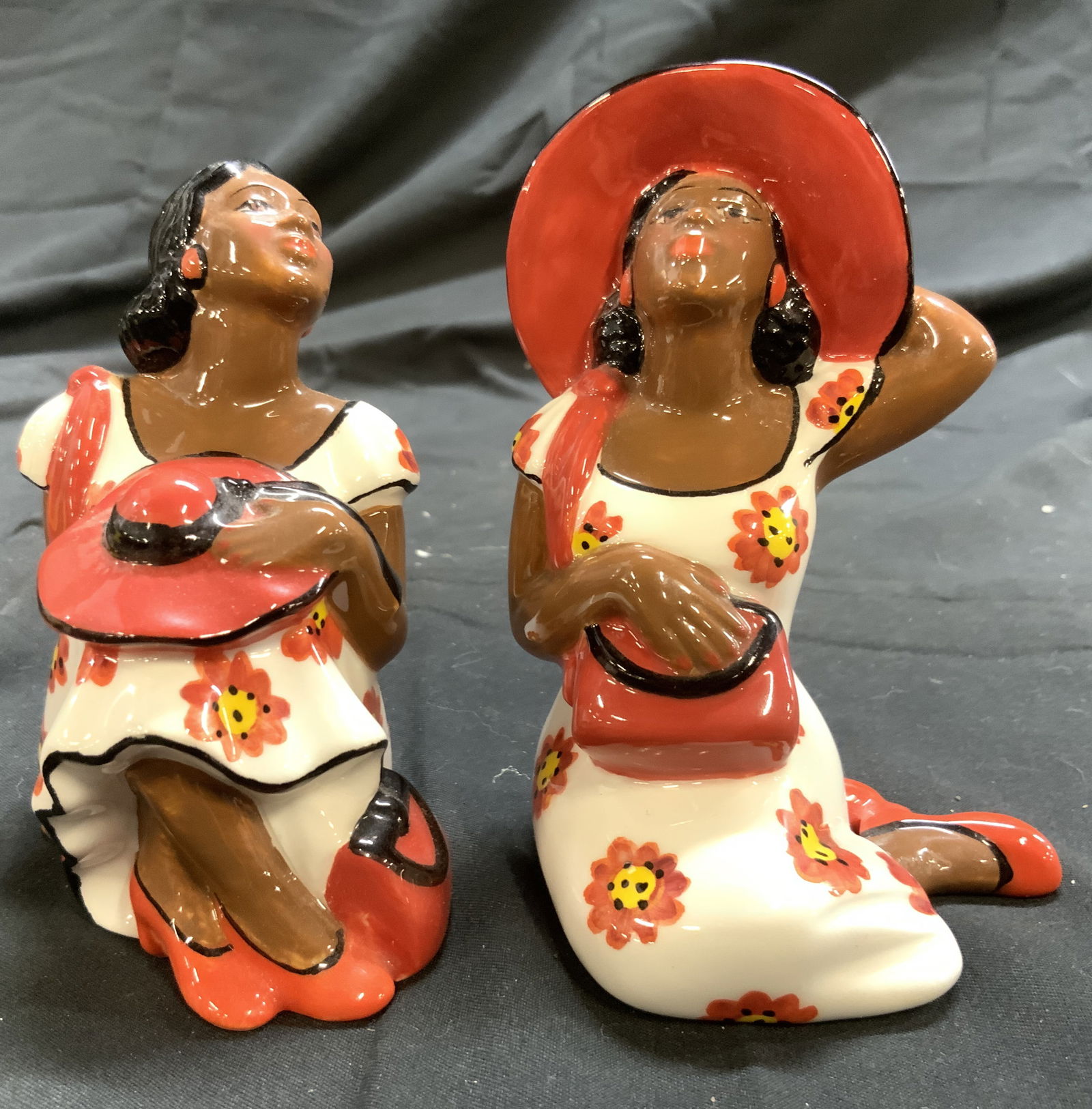 CLAY ART Porcelain Female Figure S&P Shakers: Tags on undersides read CLAY ART. Lot includes 1 salt & 1 pepper shaker. Each piece depicts female figure wearing floral detailed dresses. One holding hat, 1 wearing hat. Slightly larger shaker measur