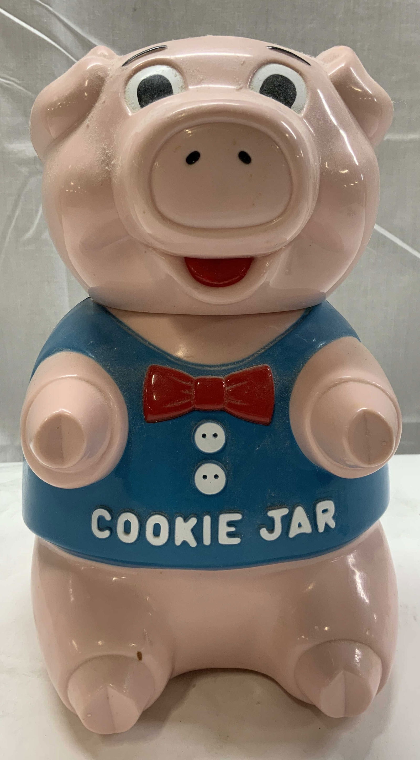 The Original Oinking Pig Cookie Jar: The Original Oinking Pig Cookie Jar Cookie jar in the shape of a pink pig wearing a blue shirt with a red bow tie. Cookie jar plays music but has not been further inspected. Signed & marked. Surface w