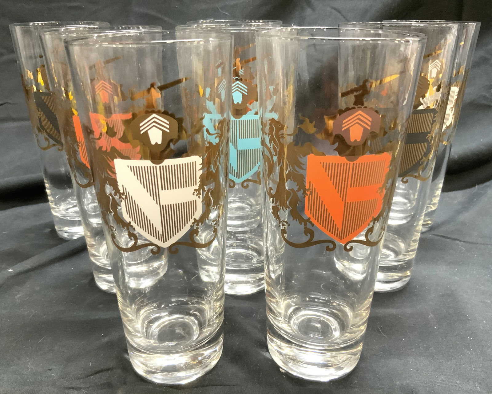 8 Mid Cntry Federal Gls Coat of Arms Highball Gls: Lot includes 8 glasses. Each coat of arms detail. With gilt areas, shelf includes light blue, red, white and slate. Each are highball glasses. Mid-Century Federal Glass Camelot Coat of Arms Highball G