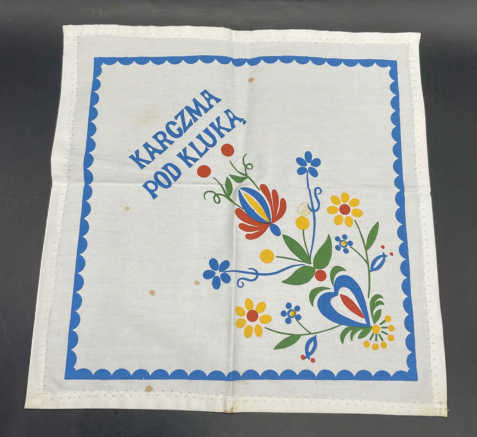 KARCZMA POD KLUKA Floral Table Napkin: KARCZMA POD KLUKA Floral Table Napkin. Multicolored floral motif to the obverse. Measures approx. 11.5L x 11.25W in. Not material tag, crafted from soft hand material. Discoloration and surface wear p
