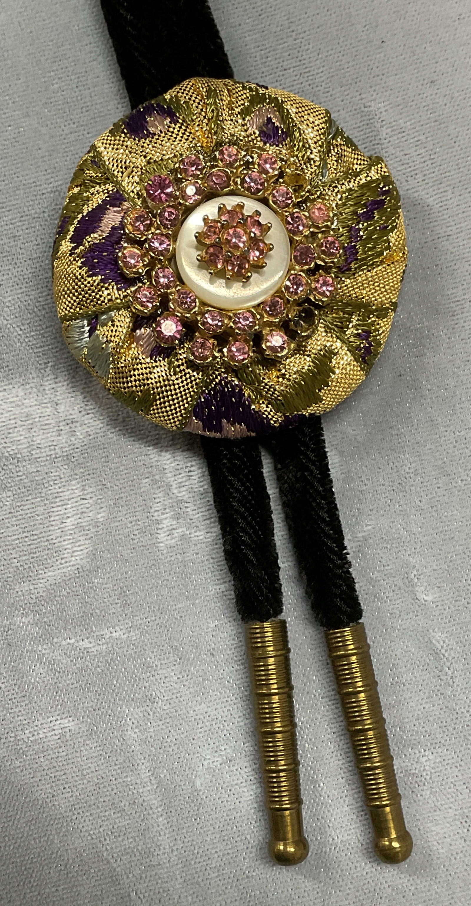 Gold Tone Pink Crystal Lariat Necklace: Black velvet lariat with gold tone tips and gold tone fabric covered pendant with pink crystal decorated flower motif. Drop length approx 19.5 inches. Pendant approx 2 inches wide. Some wear including