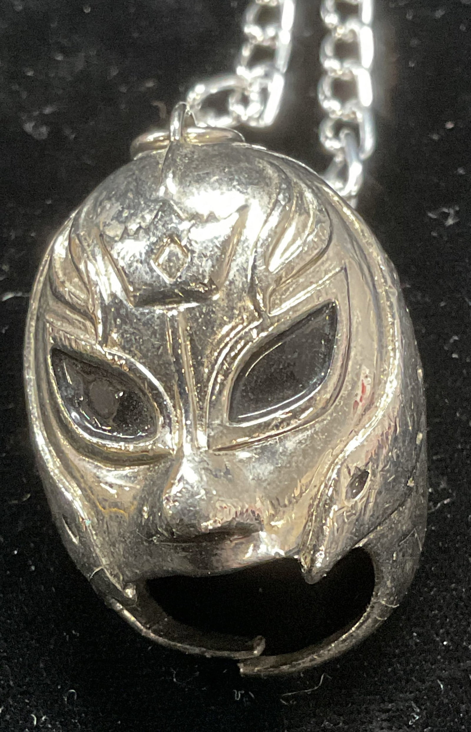 Silver Tone Luchador Pendant Necklace: Silver tone luchador mask pendant on silver tone chain. Pendant measures approx 1.5 x 1 inches. Chain drop approx 10 inches. Some wear including scratching observed. Pendant needs repair at base. Jewe