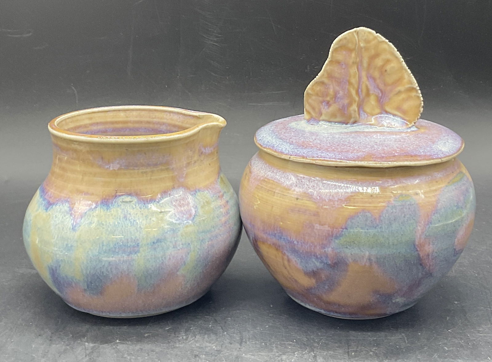 Set 2 HUNTLEY 1985 Porcelain Sugar Bowl & Creamer: HUNTLEY 1985 Handcrafted Porcelain Lidded Sugar Bowl & Creamer. Multicolored glaze. The undersides are signed HUNTLEY 85. Comes with a HUNTLEY PORCELAIN pamphlet. Finial to the sugar bowl lid has a ha