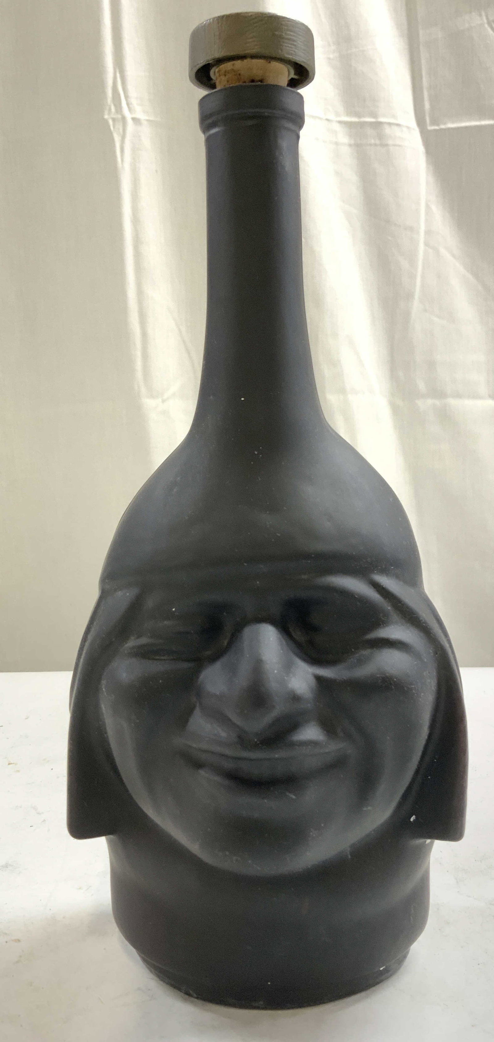 RANUZZI INCA PISCO Glass Decanter Bottle: Backside reads LIMA PERU. Underside reads Ranuzzi. Inca Pisco decanter. Piece is black toned tribal head figure. Decanter has cork stopper. Piece measures 11 inches tall 4.5 inches wide. Decanter, pis