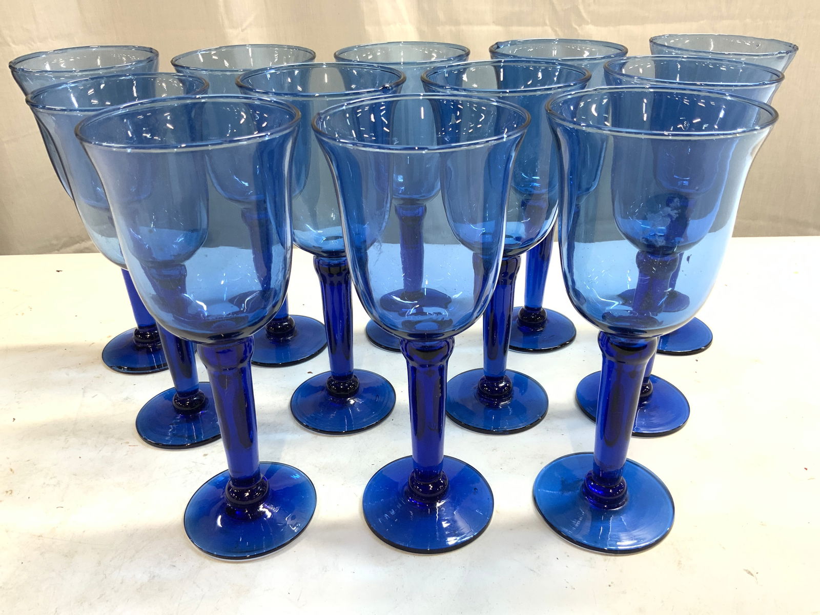 Set 12 Hand Blown Art Glass Goblets Blue: Lot includes 12 goblets. Each are blue toned. Goblets appear to possibly be hand blown due to slight variations in structure. Goblet rims lean slightly outward. Each goblet measures approx 8.5 inches