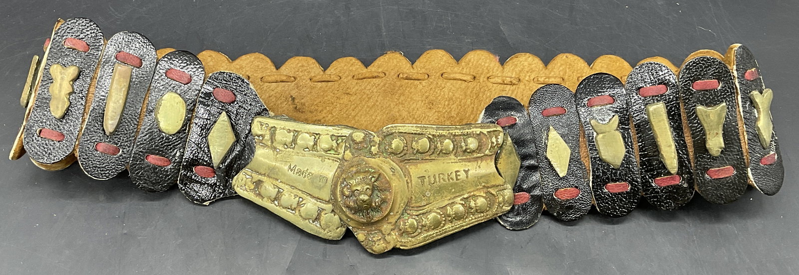 Vintage Turkish Leather & Brass Lion Motif Belt: Vintage Turkish Leather & Brass Lion Motif Belt. Obverse reads MADE IN TURKEY. Black and read paneled leather design. Raised lion head motif to the obverse. Length measured end to end approx. 31.25 in