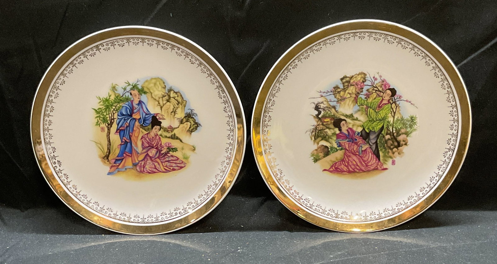 Pair EME Asian Figural Porcelain Plates, Spain: Pair of EME Asian figural motif porcelain plates with gilt rims. Measure approx 7.75 inches. Signed on undersides. Made in Spain. Both pieces have some wear consistent with exposure. EMe plate, porcel