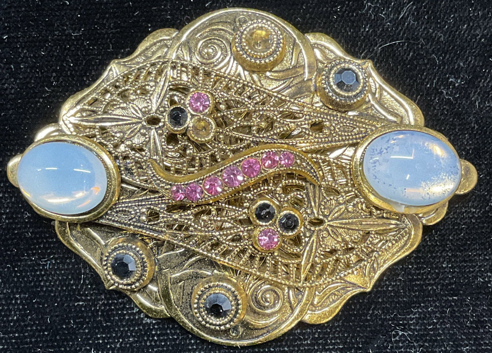 Vintage Gold Tone Filigree Crystal Brooch: Vintage gold tone brooch with filigree detail, crystal, and faux moonstone cabochons. Hinge pin to underside. Measures approx 1.75 x 2.5 inches. Some wear including scratching and losses observed. Jew