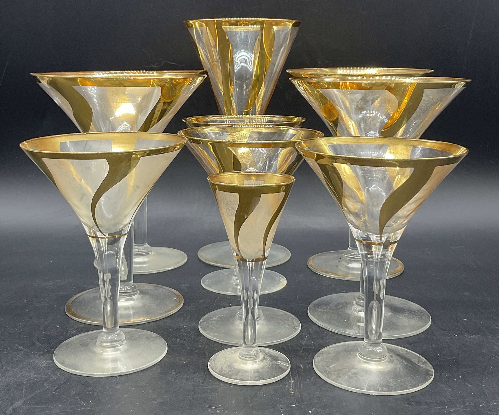 Set 10 Art Glass Gilt Rim Swirl Design Stemware: Set of 10 Art Glass Gilt Rim Stemware. Gilt design trails away from the rim in a swirl towards the stem. Various sizes. Tallest measures approx. 7.5H x 3.75W in. Losses to paint, residue, and surface 