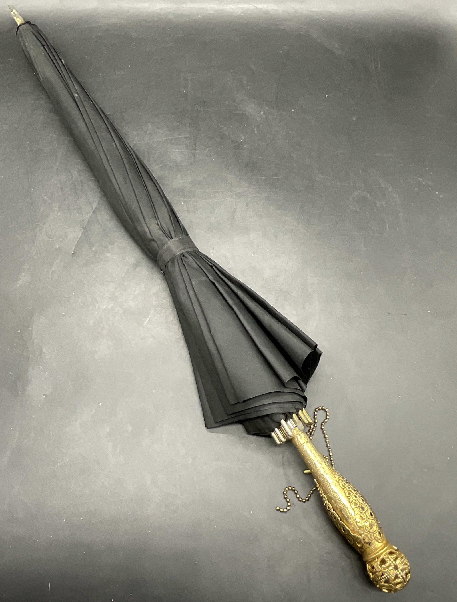 Vintage Black Umbrella W/ Ornate Gold Tn Handle: Vintage Black Fabric Umbrella With Ornate Gold Tone Handle. Ball chain attached to the handle. Measures approx. 24.5L x 2W in. Measured closed. Losses to finish, losses to fabric, missing interior pie