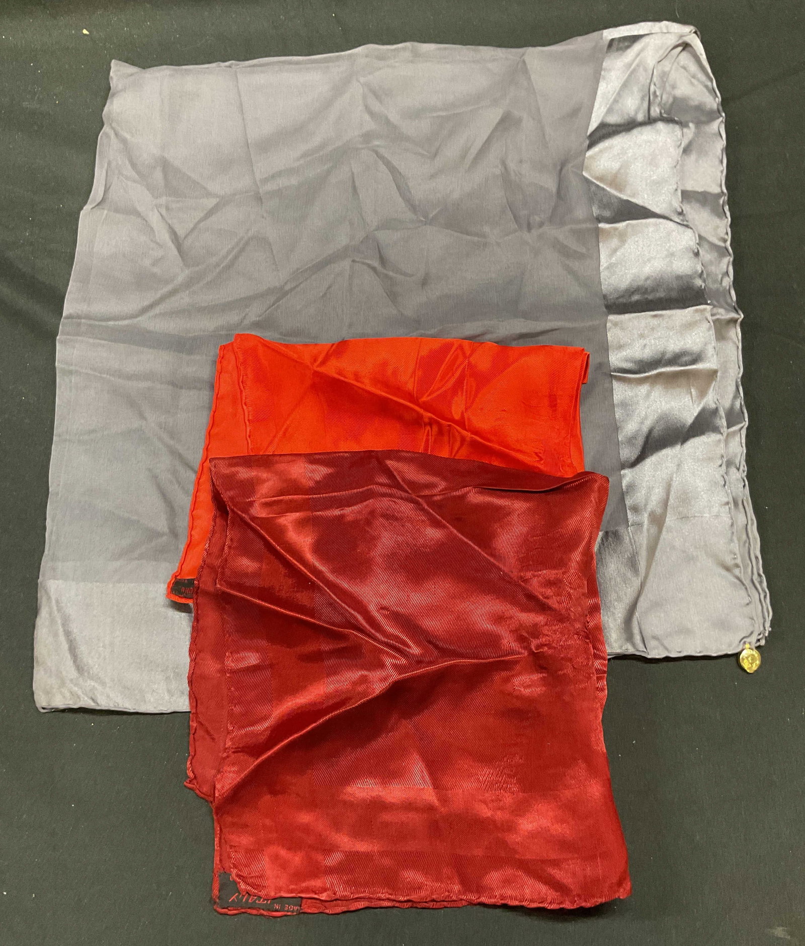Lot 3 Scarves, Rhodia Italia Red Italy +: Lot of 3 red and grey silk and acetate scarves. 2 Rhodia Italia red acetate scarves, made in Italy. 1 sheer grey silk scarf. Largest scarf measures approx 30 x 30 inches. All pieces have wear includin