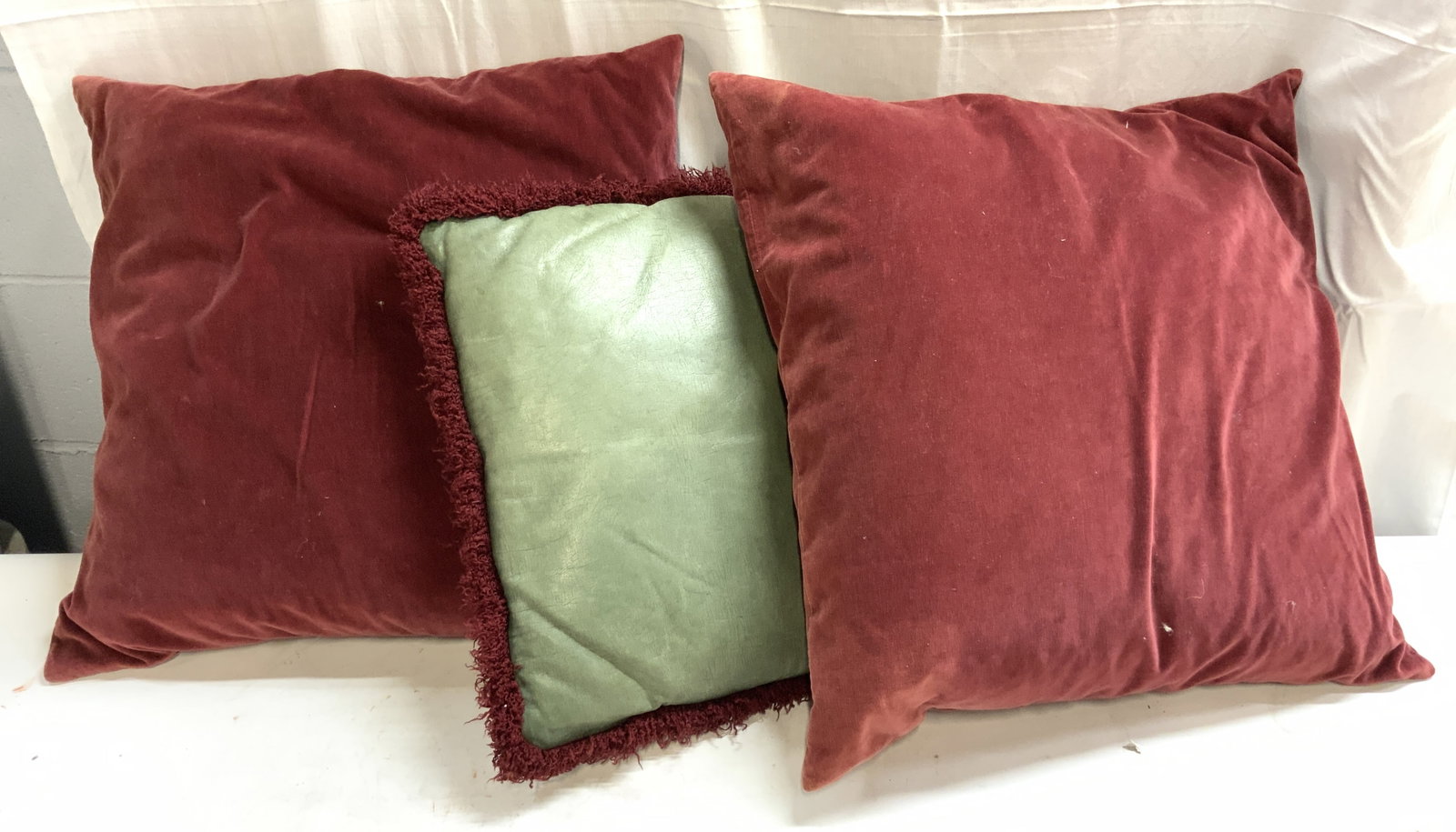 Lot 3 Down & Leather Pillows: Lot includes 2 cranberry toned down pillows & 1 green toned leather pillow with fringes (appears to be genuine leather possibly leatherette) Largest measures approx 19 inches square. Pillows, throw pi
