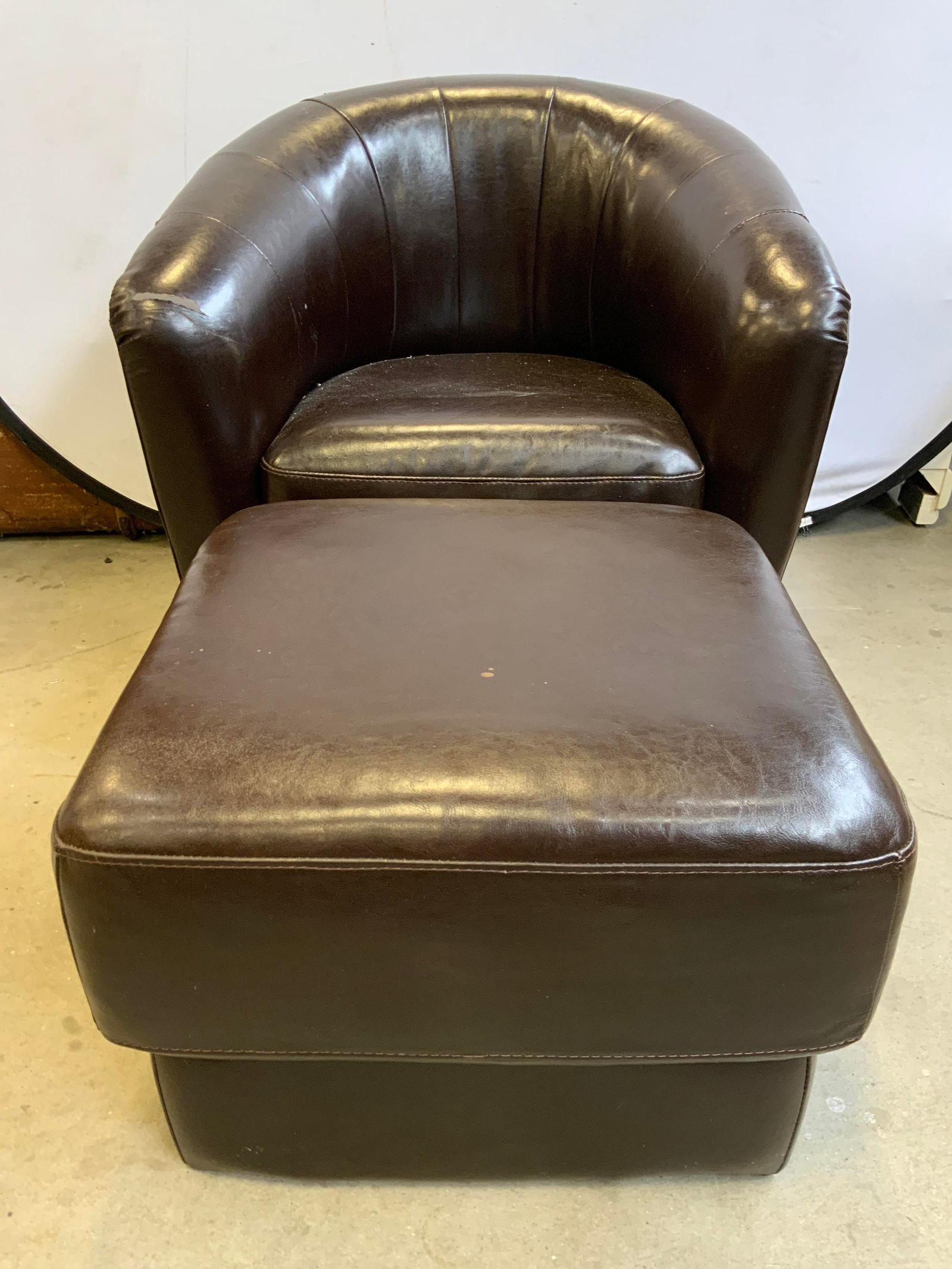 Set Leatherette Upholstered Armchair & Ottoman: Lot includes 1 swivel armchair and 1 ottoman. Each piece is brown toned upholstered with leather style material. Ottoman has wooden feet. Armchair measures approximately 30 inches deep 32 inches wide 