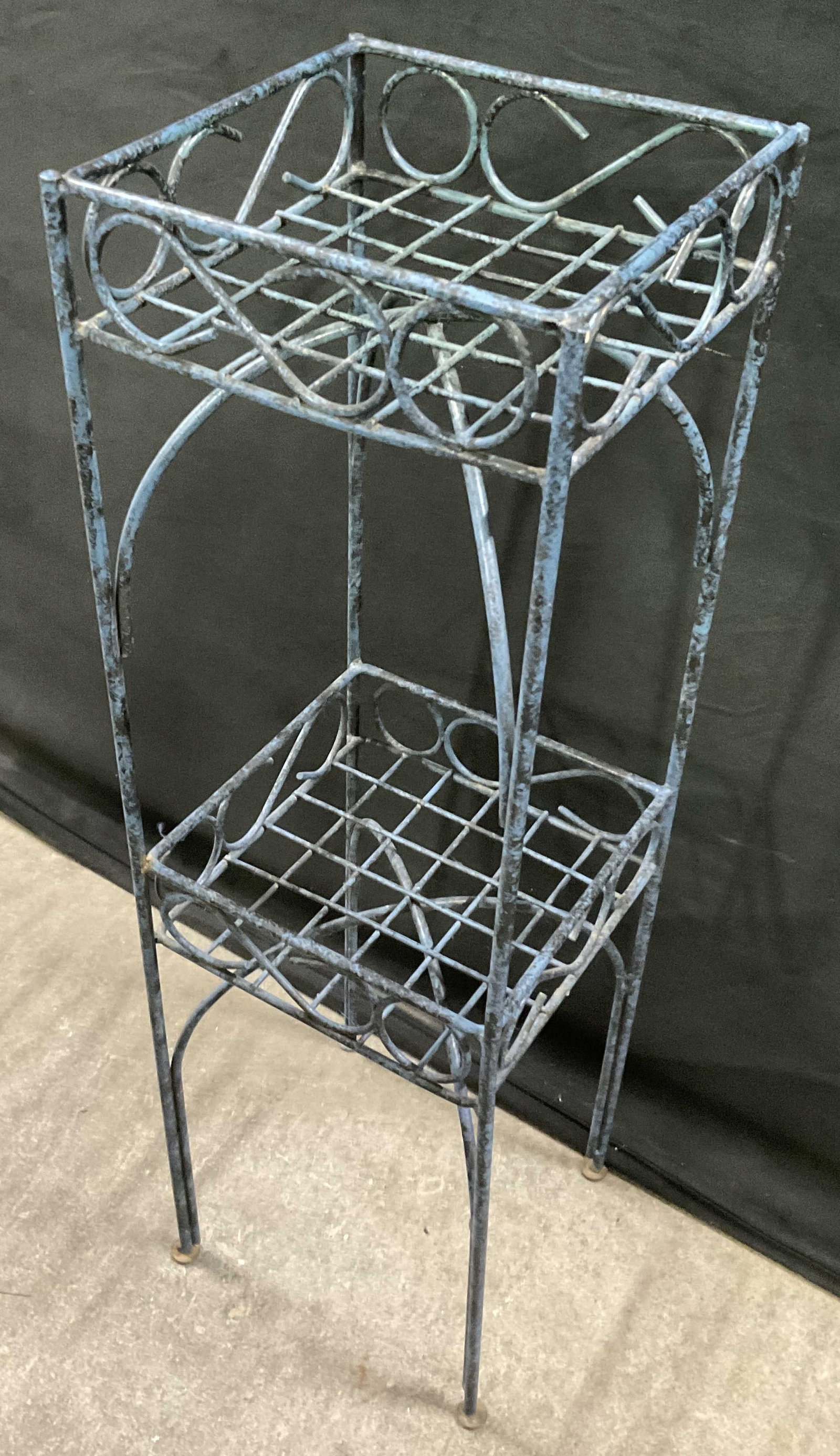 Vintage Metal Two Tiered Plant Stand: Vintage Metal Two Tiered Plant Stand. Black and blue hued finish to the piece. Scrolled and open metalwork designs throughout. Measures approx. 28.25H x 8.25W x 8.25D in. Surface wear consistent with 