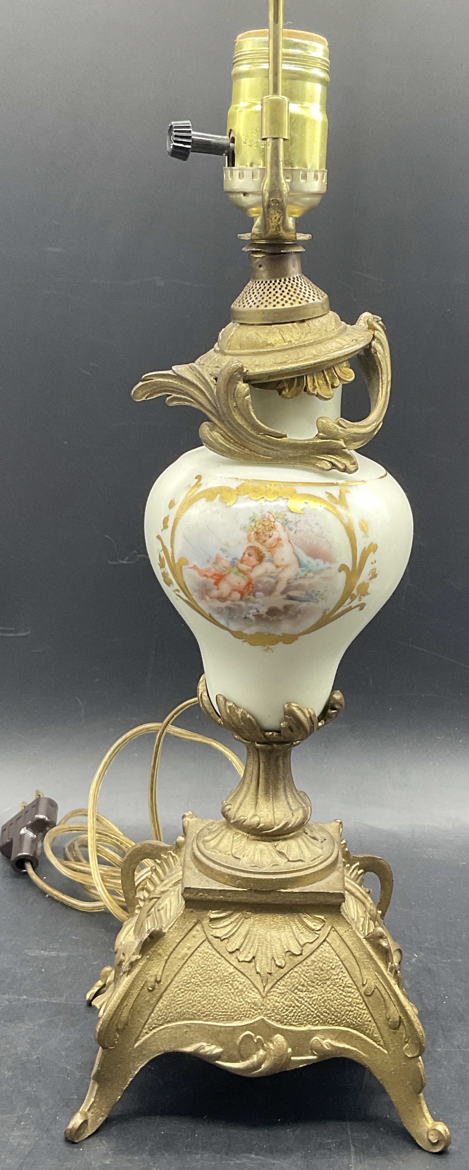 Vintage Hand Painted Putti Motif Porcelain Lamp: Vintage Hand Painted Putti Motif Porcelain Lamp. Tabletop lamp crafted from metal and porcelain. Corded. Measures approx. 25H x 5.5W in. Measurement includes harp. Plastic finial to the piece. Lamp ne