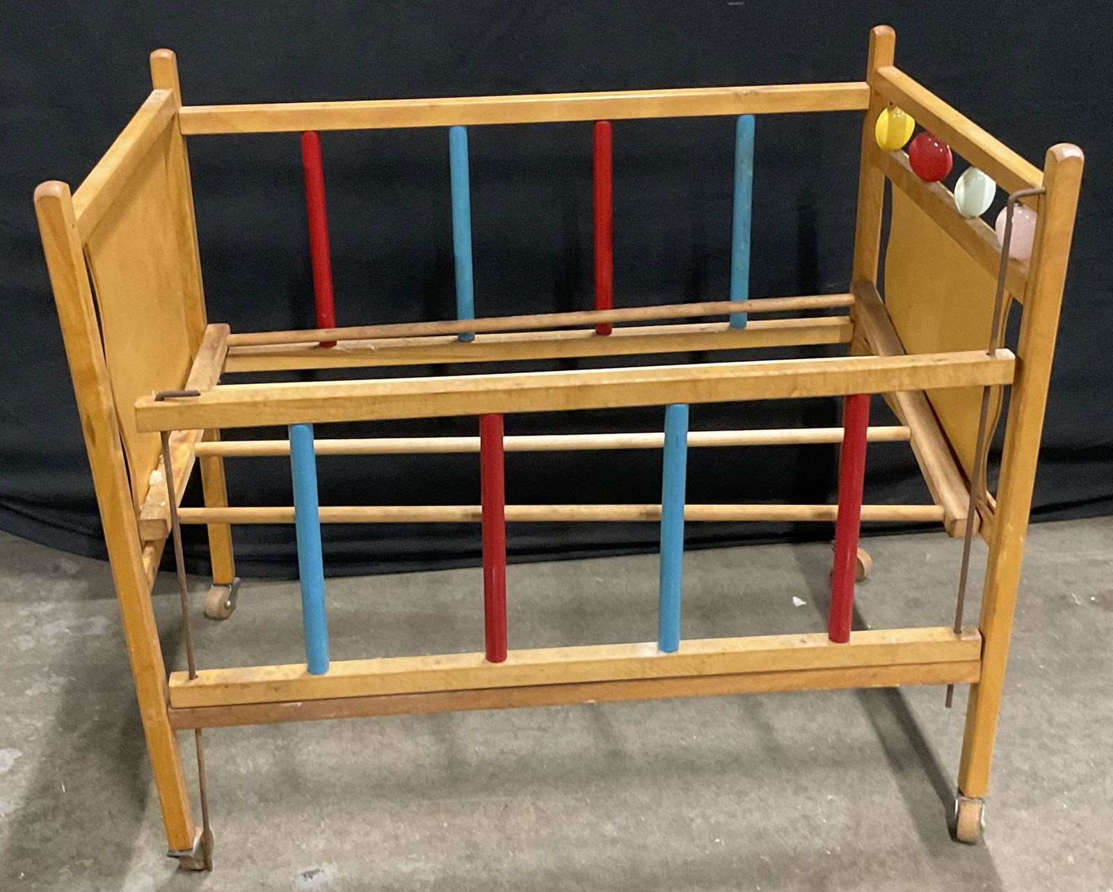 Vintage Wooden Doll Crib on Wooden Casters: Vintage Wooden Doll Crib on Wooden Casters. Primarily a light brown hue accented by red, blue, yellow, and pink hues. Rabbit sticker to one side. Metal hardware attaches casters to the crib. Measures
