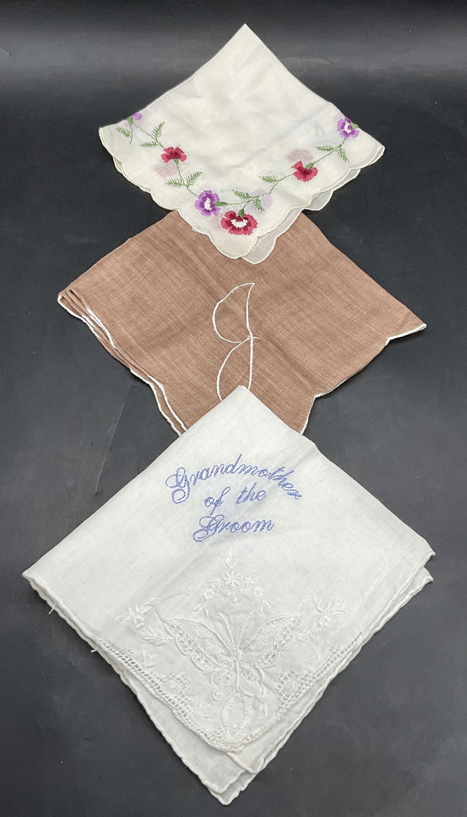 3 Floral, Bridal, Embroidery Fabric Handkerchiefs: Lot of 3 Fabric Handkerchiefs. Crafted from soft hand fabric. One embroidered floral motif hankie, one brown embroidered hankie, and hankie that reads Grandmother of the Groom. Floral hankie measures