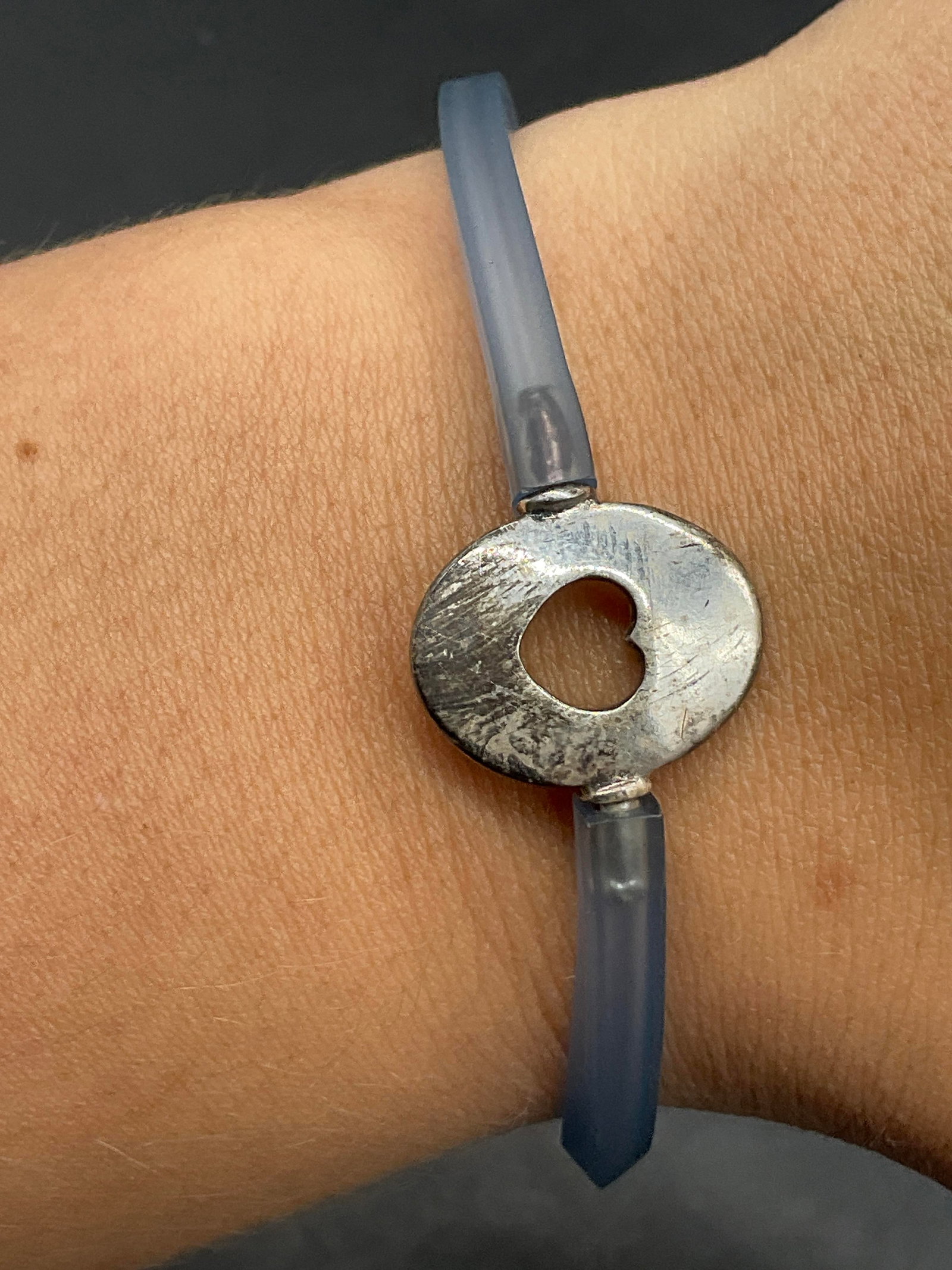 Vintage Silver Tone Metal Heart Charm Bracelet: Blue rubber bracelet with a silver tone metal heart motif charm to the center. The charm functions as the clasp as the rubber attaches to it. Measures approx. 7.75 inches in length. Surface wear consi