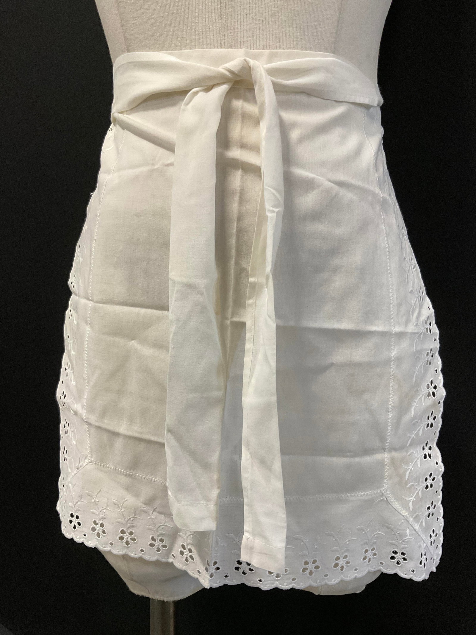 Vintage White Floral Motif Fabric Tie On Apron: Vintage White Floral Motif Fabric Tie On Apron. Pierced fabric details to the piece. Measures approx, 82W x 16L in. Width Includes the straps that would be tied to secure the apron. Discoloration, loo