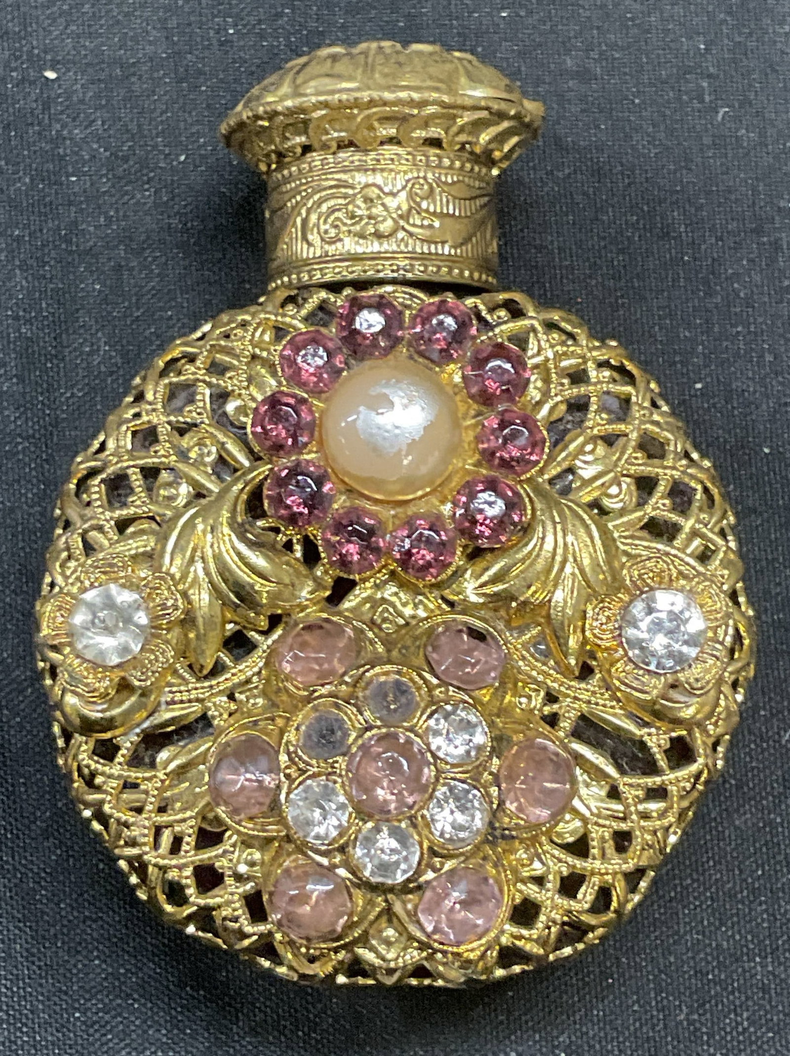 Vtg Gold Tone Glass Bejeweled Perfume Bottle: Vintage purple glass perfume bottle with gold tone filigree cover and bejeweled crystal and faux pearl decoration. Measures approx 2.5 x 1.5 inches. Some crystals need replacement. Perfume bottle, bej