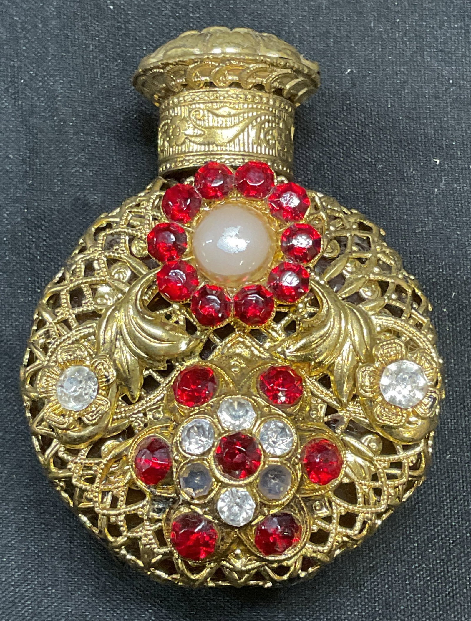 Vtg Gold Tone Glass Bejeweled Perfume Bottle: Vintage Amber glass perfume bottle with gold tone filigree cover and bejeweled crystal and faux pearl decoration. Measures approx 2.5 x 1.5 inches. Some crystals need replacement. Perfume bottle, beje
