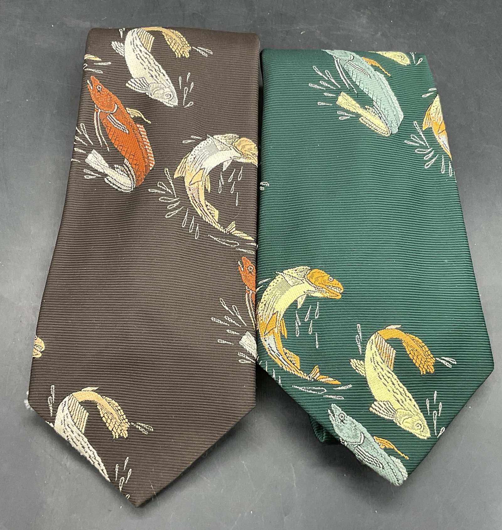 Lot 2 Vintage Brown & Green Fish Motif Ties: Lot 2 Vintage Brown & Green Fish Motif Ties. Brown tie measures approx. 54L x 4W in. Pieces are crafted from polyester. Surface wear consistent with age, use, and exposure. Wearables, fashion, fashion