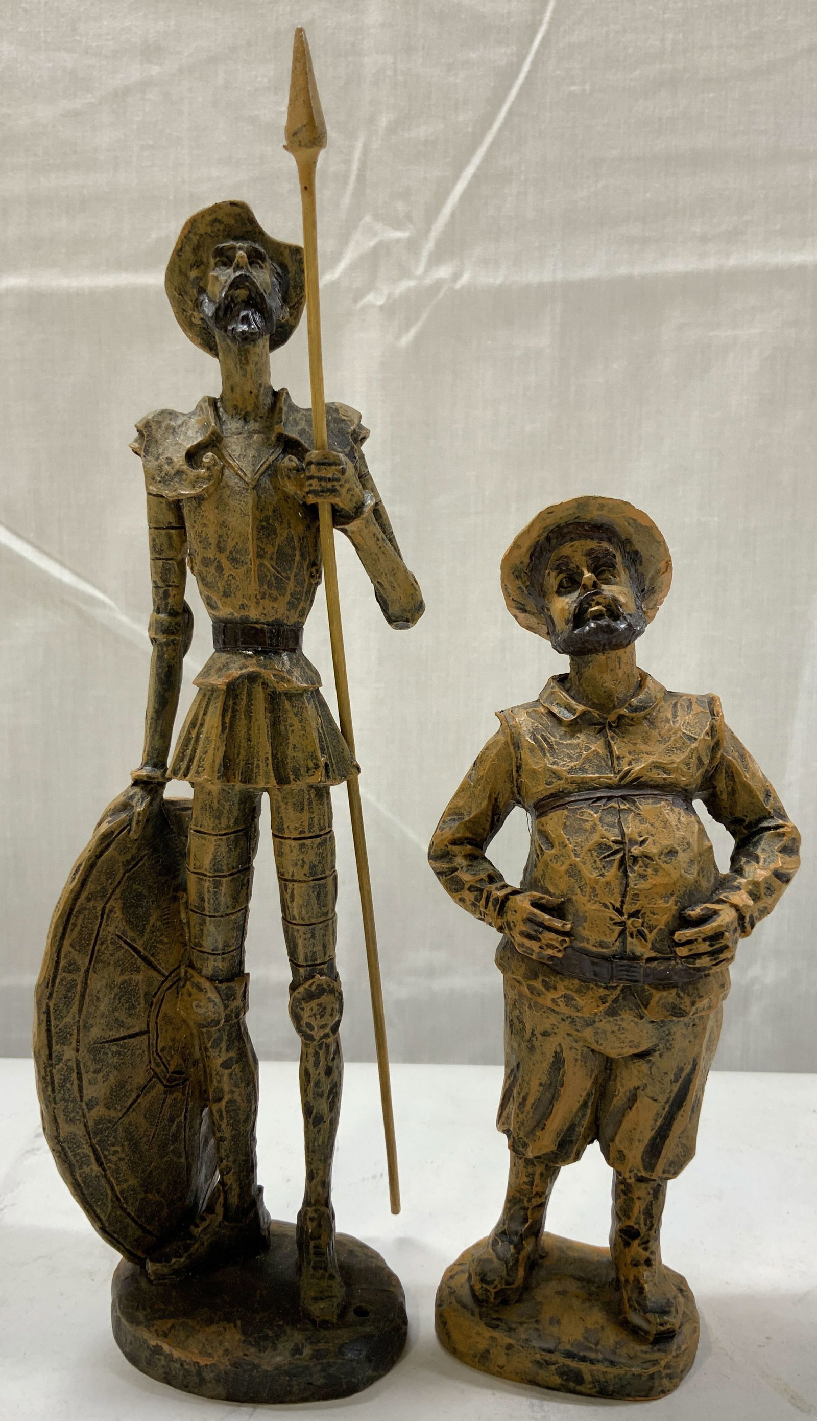 2 Brown Don Quixote & Sancho Panza Figurines: 2 Brown Don Quixote & Sancho Panza Figurines Don Quixote figurine is wearing knight attire & holding a spear & a shield. Sancho Panza figurine is wearing a hat & appears to be looking up. Surface wear