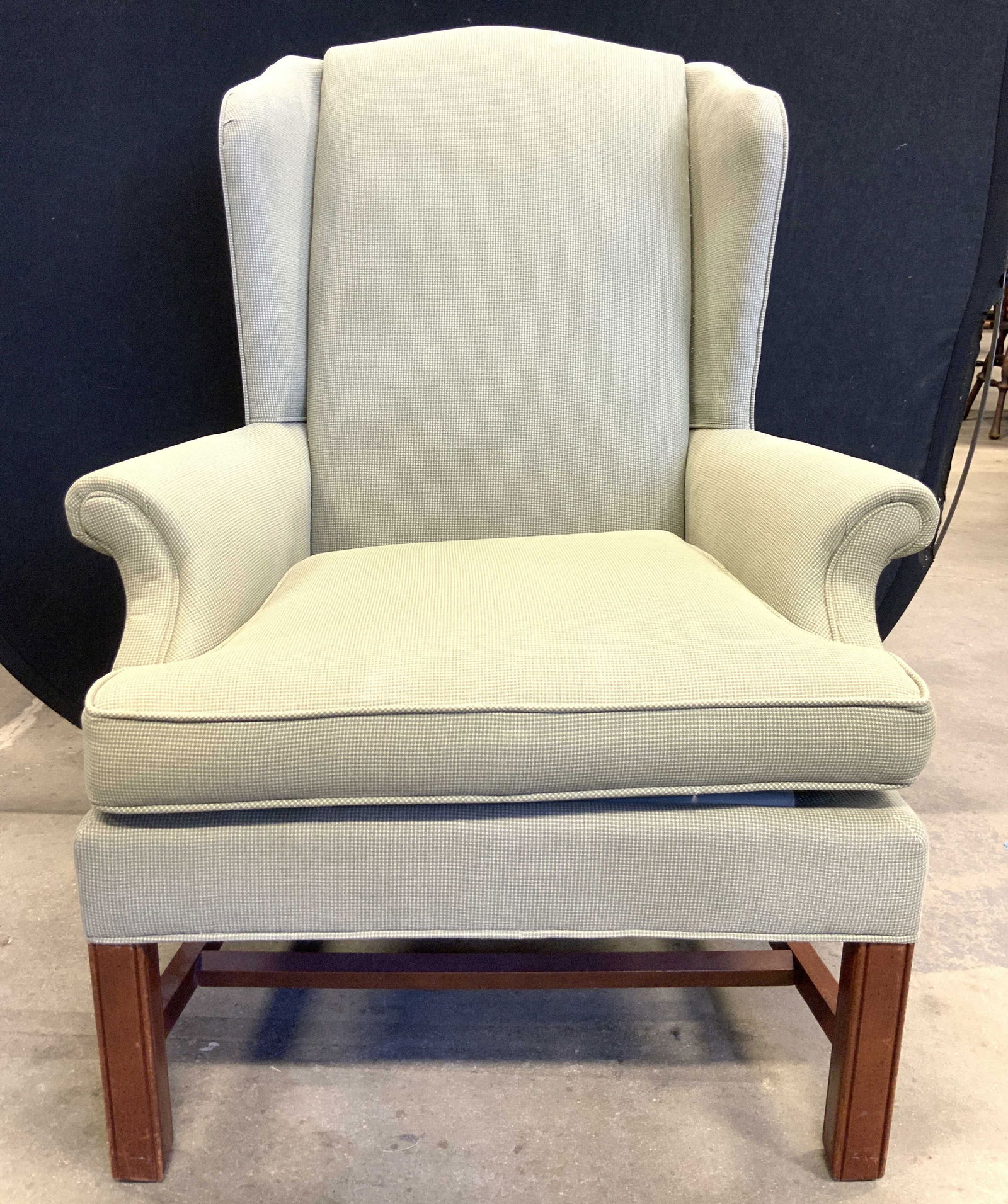 Vintage Wingback Armchair W Wooden Legs: Armchair is vintage. Piece is upholstered in light green toned fabric. Chair has winged backrest. Piece has light brown toned wooden legs with stretchers in between. Piece measures approximately 40 in